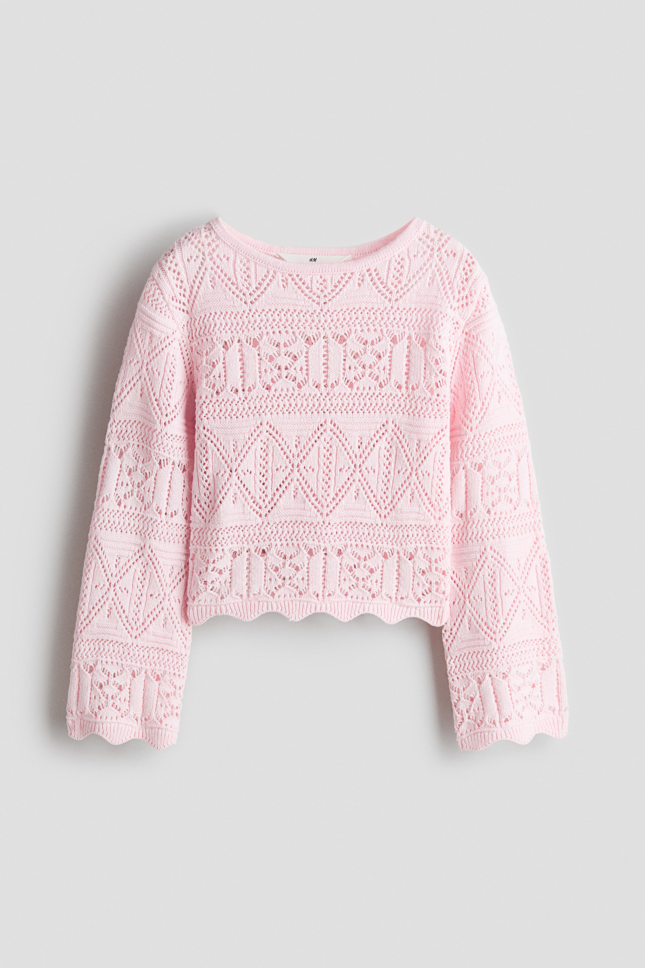 Ingrandisci l'immagine: Un maglione corto rosa è presentato dal FRONTE, caratterizzato da una morbida maglia traforata con un aspetto all'uncinetto e un intricato motivo a giorno. È progettato con uno scollo rotondo, spalle scese, maniche lunghe e bordi a coste smerlati ai polsi e all'orlo.