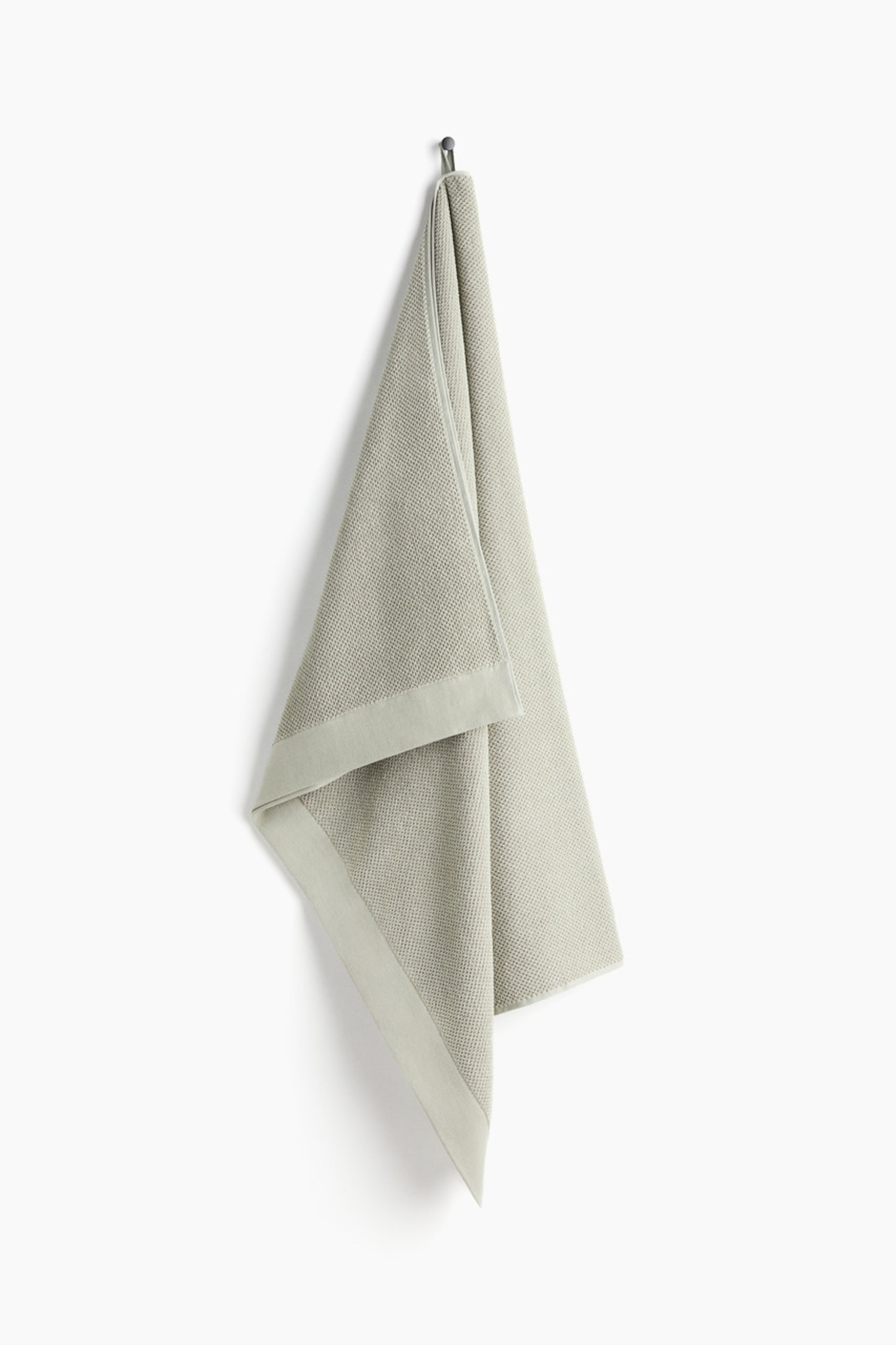 View larger image: A light green classic bath sheet is hanging vertically from a hook, showcasing a textured main surface and a smooth, flat border along its edges, with a fabric loop visibly securing it at the top.