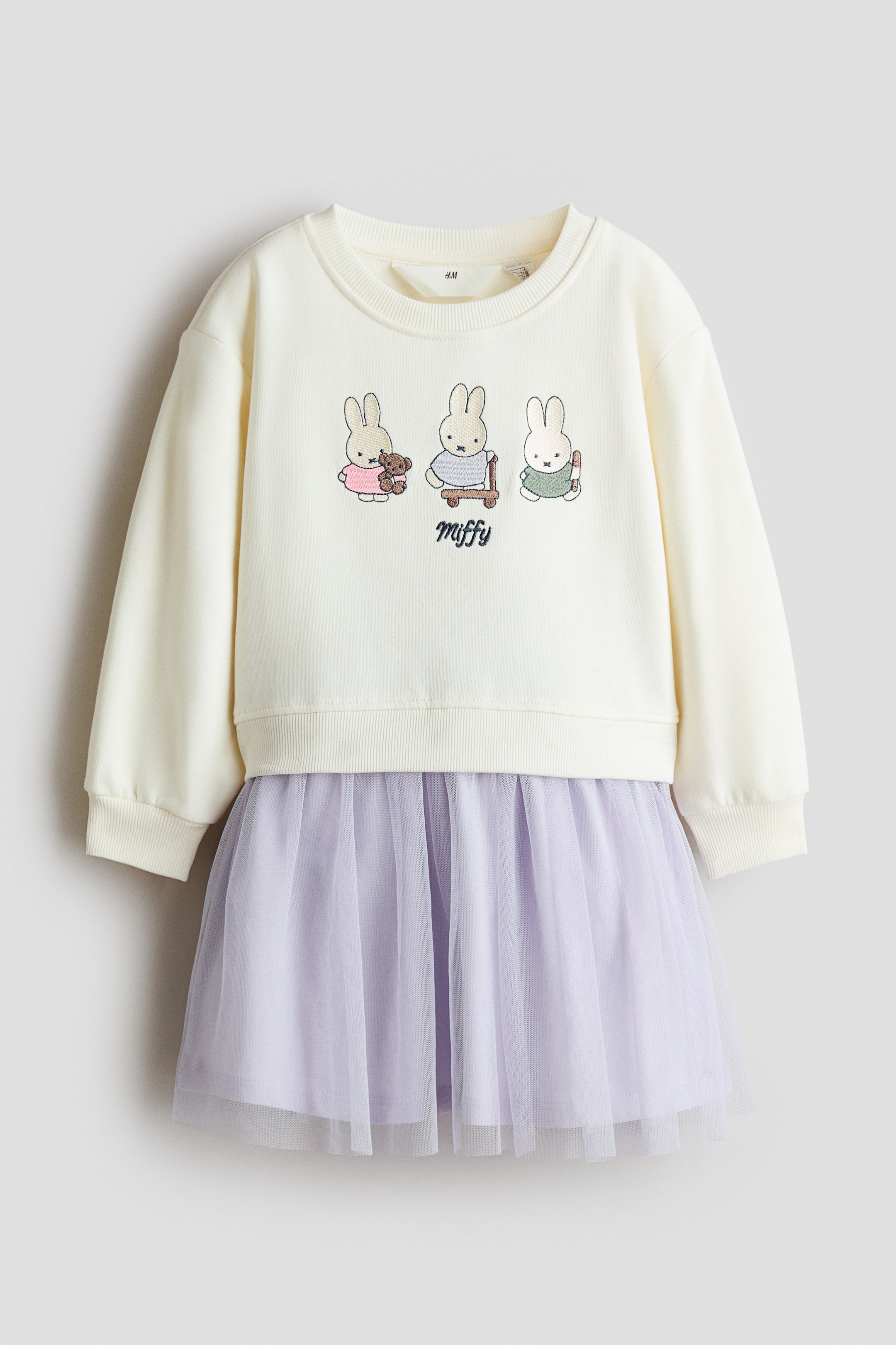 Größeres Bild ansehen: Ein Kinderkleid wird von vorne gezeigt, mit einem cremefarbenen Sweatshirt-Oberteil mit drei aufgedruckten Miffy-Figuren auf der Brust und einem angesetzten hellvioletten Tüllrock. Das Sweatshirt verfügt über einen gerippten Rundhalsausschnitt, überschnittene Schultern, lange Ärmel mit gerippten Bündchen und einen gerippten Saum.