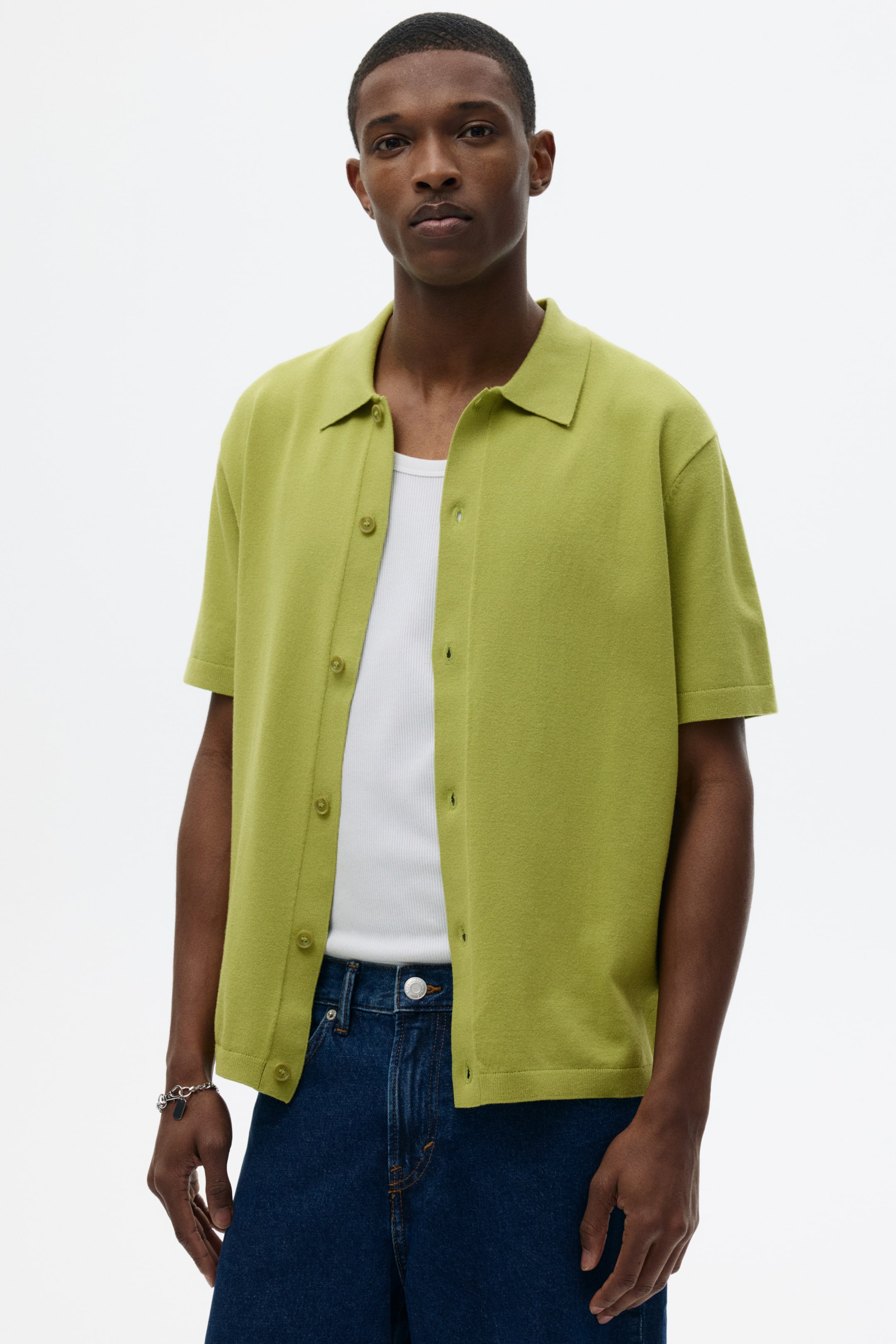 View larger image: A lime-green knit shirt features a pointed collar, short sleeves with ribbed cuffs, and a full button-front fastening with tone-on-tone buttons. It is styled open over a white ribbed tank top.