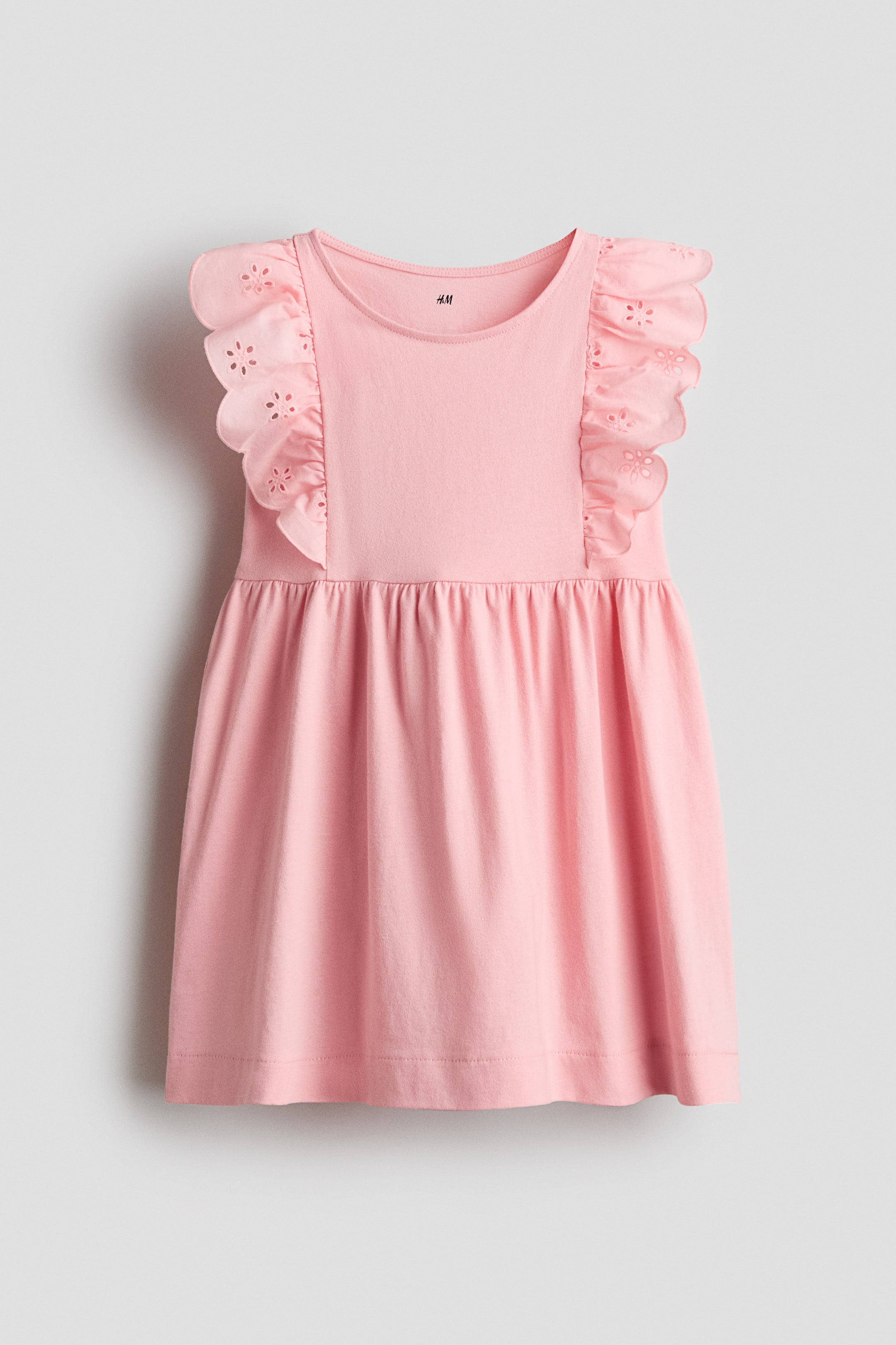 Visa större bild: En rosa klänning visas framifrån, med en rund halsringning och rynkade kapärm med vågiga kanter och broderade hålsömsdetaljer. Klänningen är rynkad i midjan och bildar en utsvängd kjol.