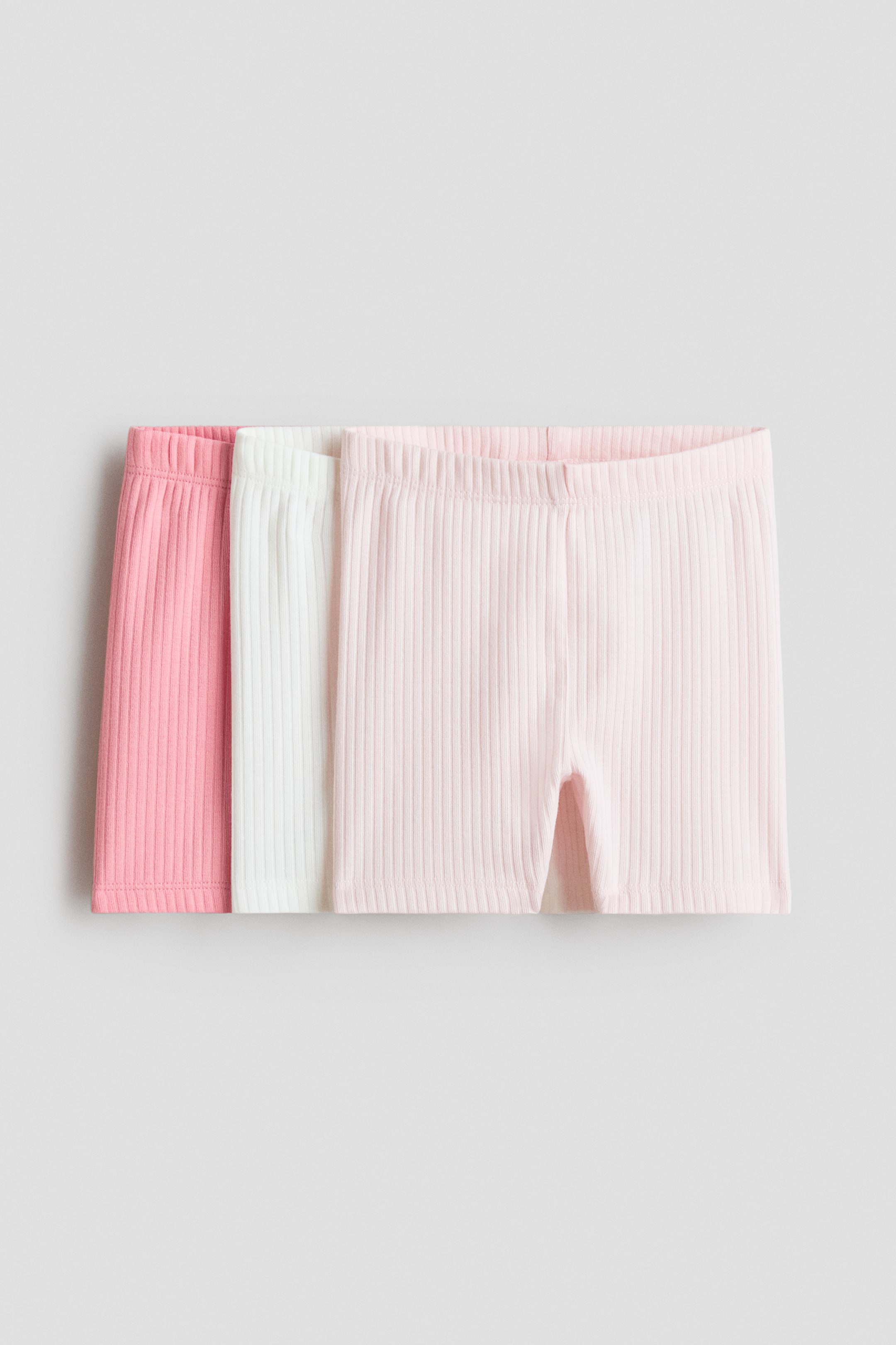 Ver imagem maior: Três pares de calções de ciclismo estão dispostos lado a lado, exibindo a parte frontal. Apresentam uma textura de jersey de algodão canelado com elástico coberto na cintura, disponíveis em rosa, branco e rosa claro.