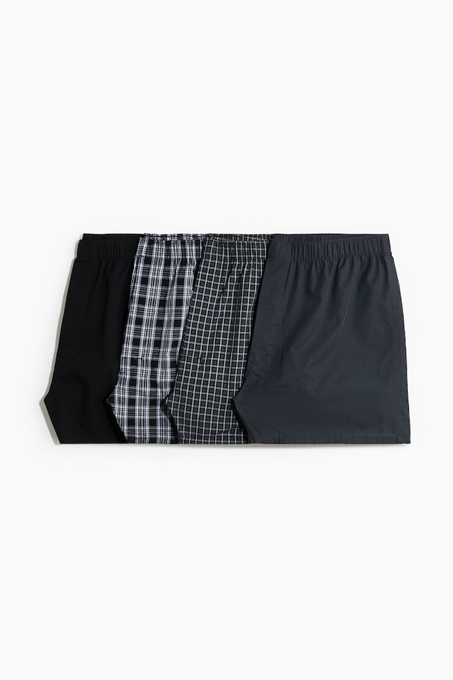 Four pairs of boxer shorts are laid out flat, side by side, each boasting an elasticated waistband. The set includes a plain black pair, a black and white checked pair, a dark grey and white small checked pair, and a dark grey pair with a subtle striped pattern. - 1