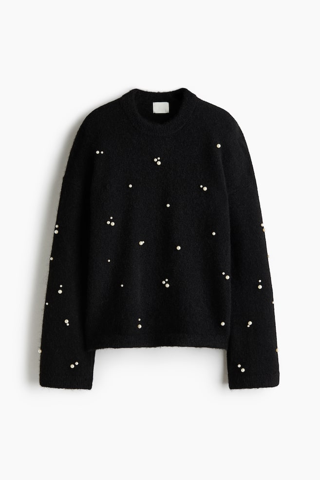 En oversized svart jumper i ett mjukt, borstat stickat material visas framifrÃ¥n, med utspridda vita sfÃ¤riska pÃ¤rlor Ã¶ver hela plaggets kropp och Ã¤rmar. Designen har en rund halsringning med ribbkant, nedsÃ¤nkta axlar och diskret ribbstickning vid Ã¤rmslut och nederkant. - 1