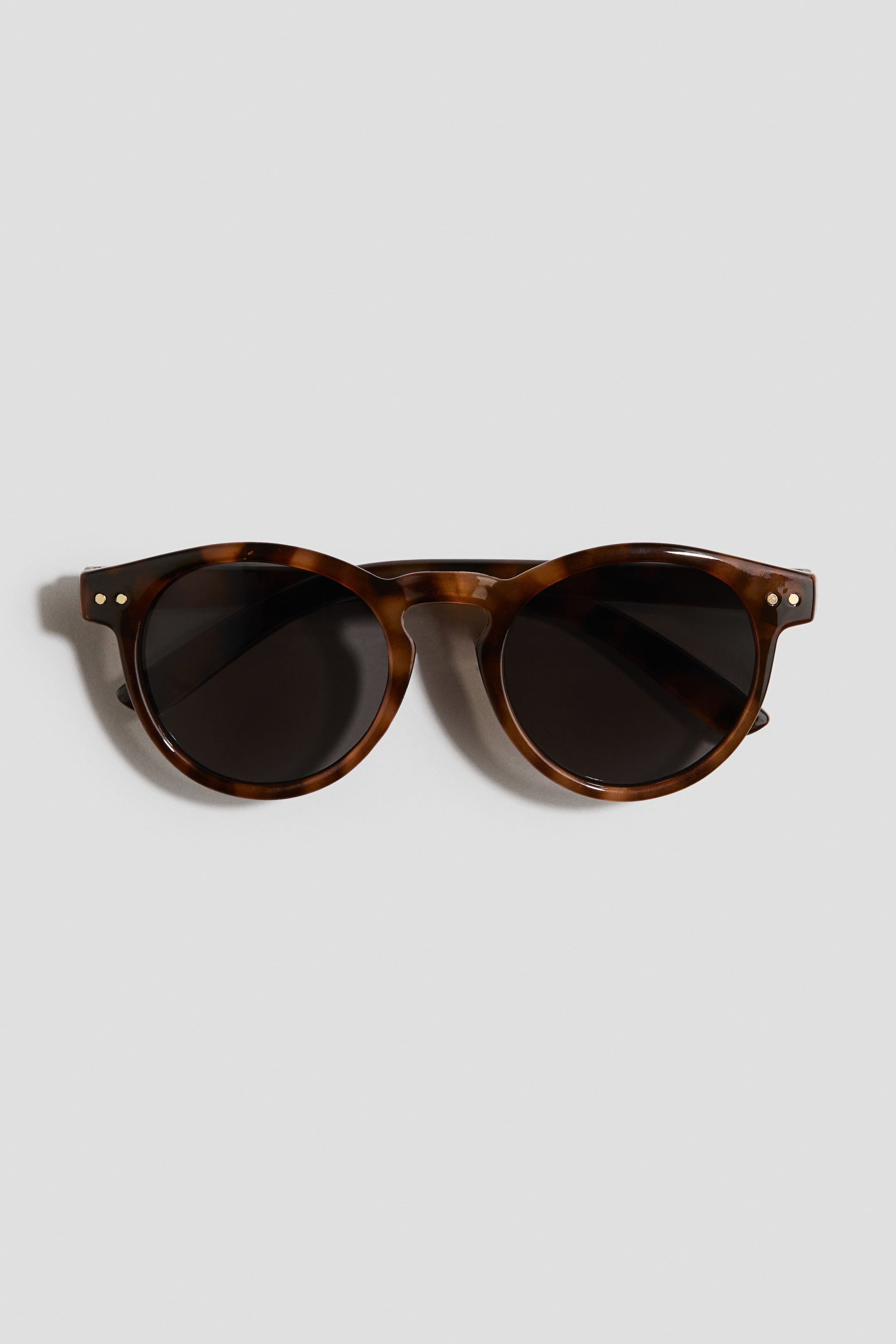 Ampliar la imagen: Gafas de sol redondas de plástico con lentes tintadas y con protección UV, que presentan un patrón carey. El FRENTE de la montura muestra pequeñas tachuelas circulares de color dorado en sus bordes exteriores.
