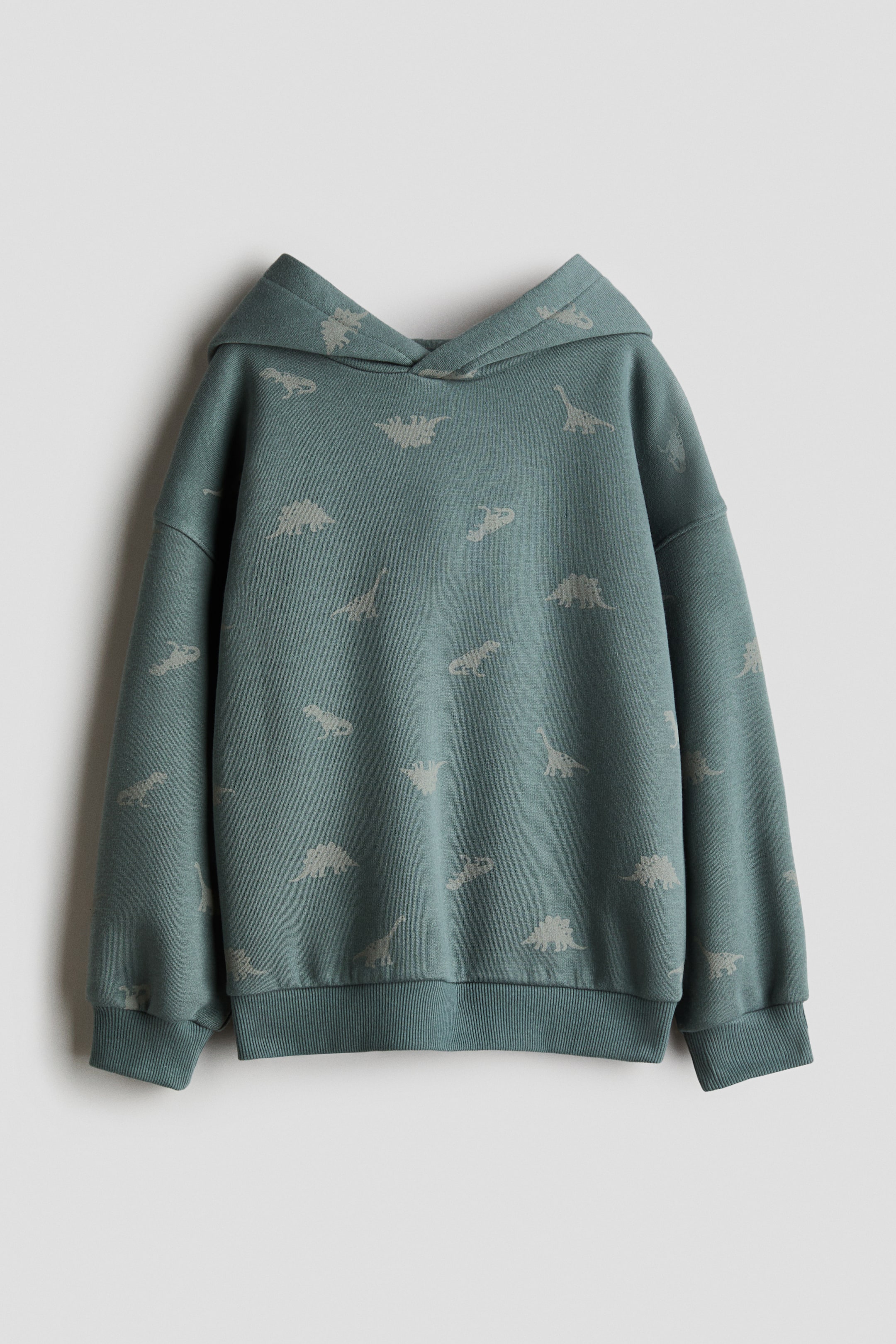 Agrandir l'image: Un sweat à capuche bleu sarcelle est posé à plat, arborant un motif intégral de silhouettes de dinosaures gris clair. Il est conçu avec une capuche, des manches longues, des poignets côtelés et un ourlet côtelé.