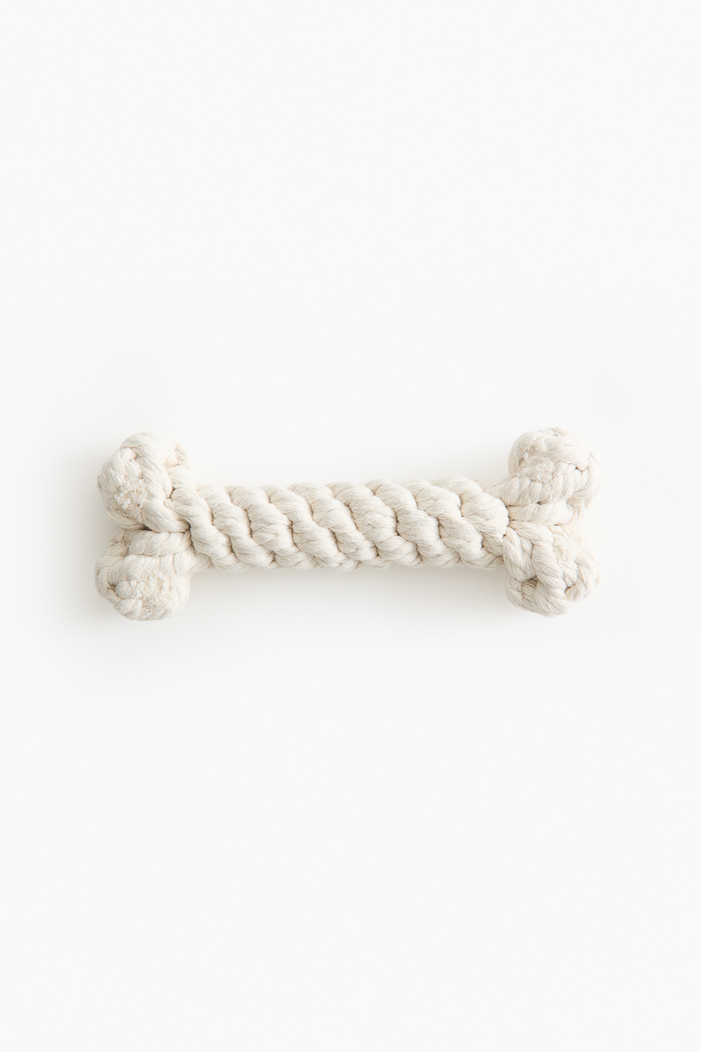 A bone-shaped pet toy made from thick, off-white braided rope is lying facing forward, showcasing its tightly knotted central shaft and rounded bulbous ends.