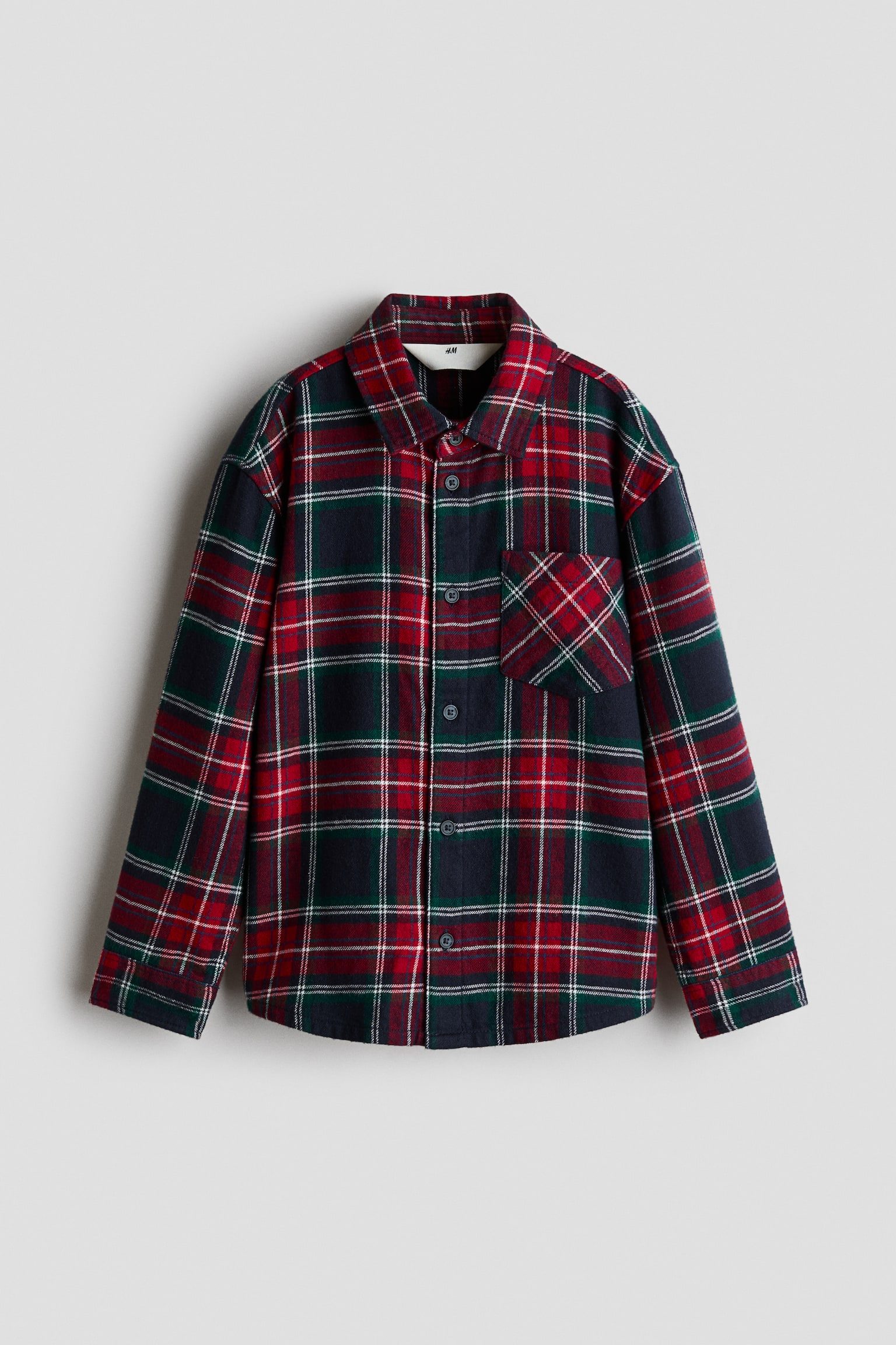 A loose-fit flannel shirt in a red, green, and navy plaid pattern is shown from the front, featuring a collar, button-down front, and dropped shoulders. The shirt has long sleeves with button cuffs, a single open chest pocket, and a gently rounded hem.