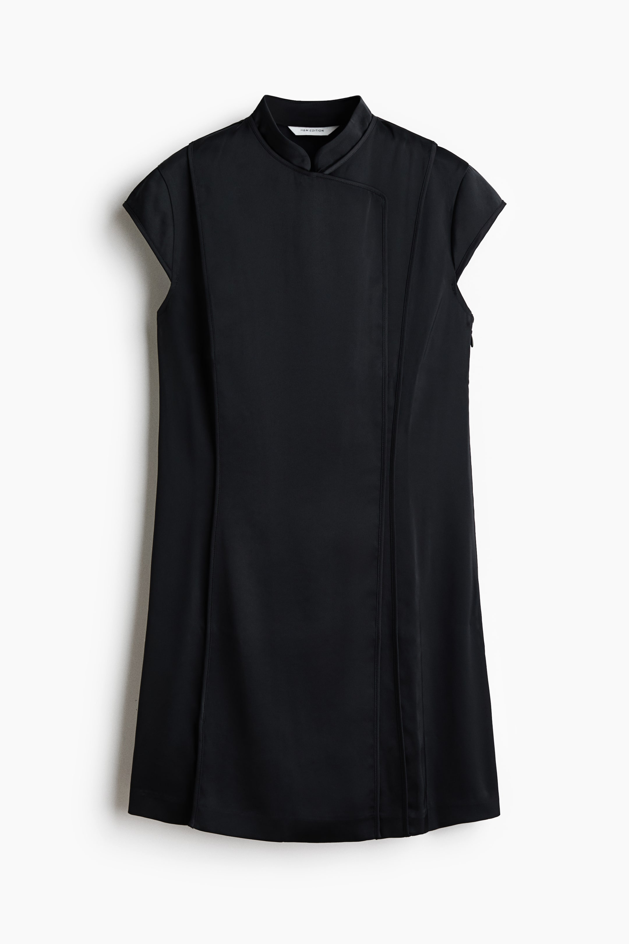 View larger image: A black dress features a mandarin collar and short cap sleeves. It has an asymmetrical overlapping front panel and prominent vertical seams running down the front.