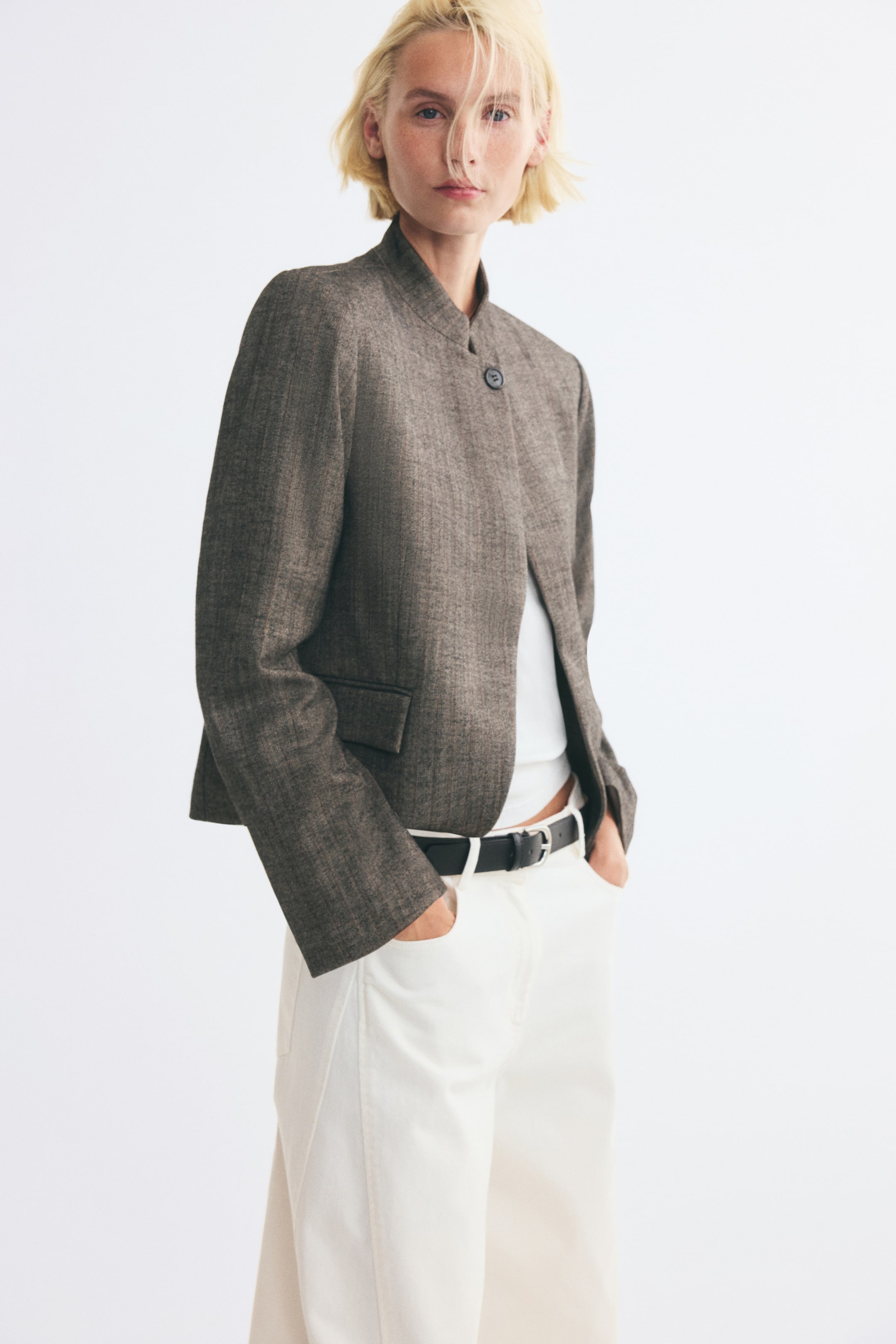Voir une image plus grande: Un blazer à boutonnage simple en tissu tissé texturé brun est porté par le mannequin par-dessus un haut blanc et un pantalon blanc. Le blazer présente un col montant avec une fermeture à un seul bouton, un décolleté sans revers, des épaules structurées et une poche avant à rabat.
