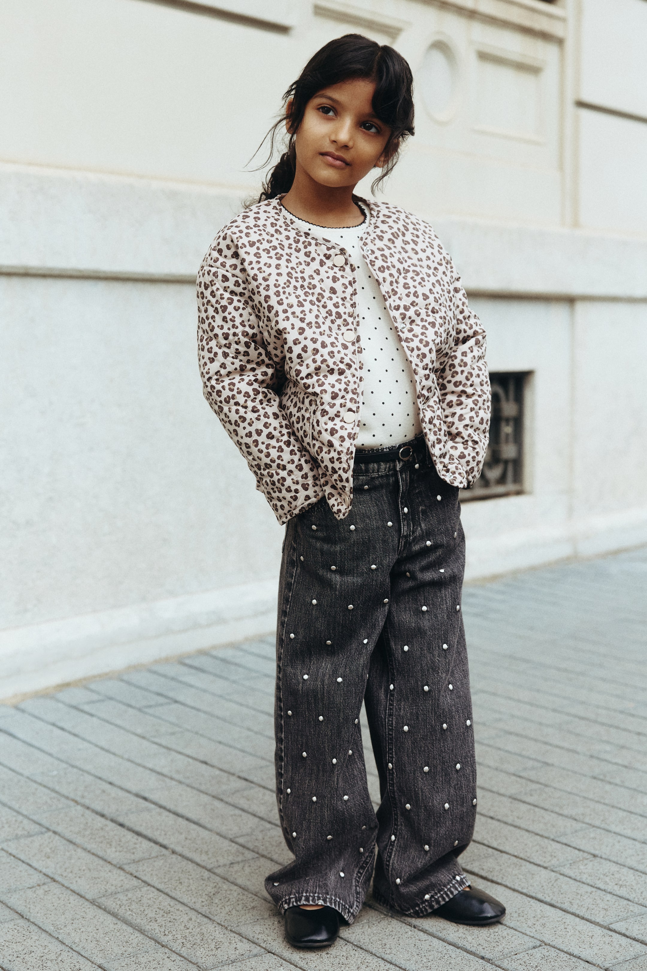 Ampliar la imagen: Jeans de pierna ancha de color negro lavado, presentados desde una vista frontal ligeramente inclinada, presentan tachuelas plateadas repartidas por el frente. Un cinturón negro está ajustando la cintura.