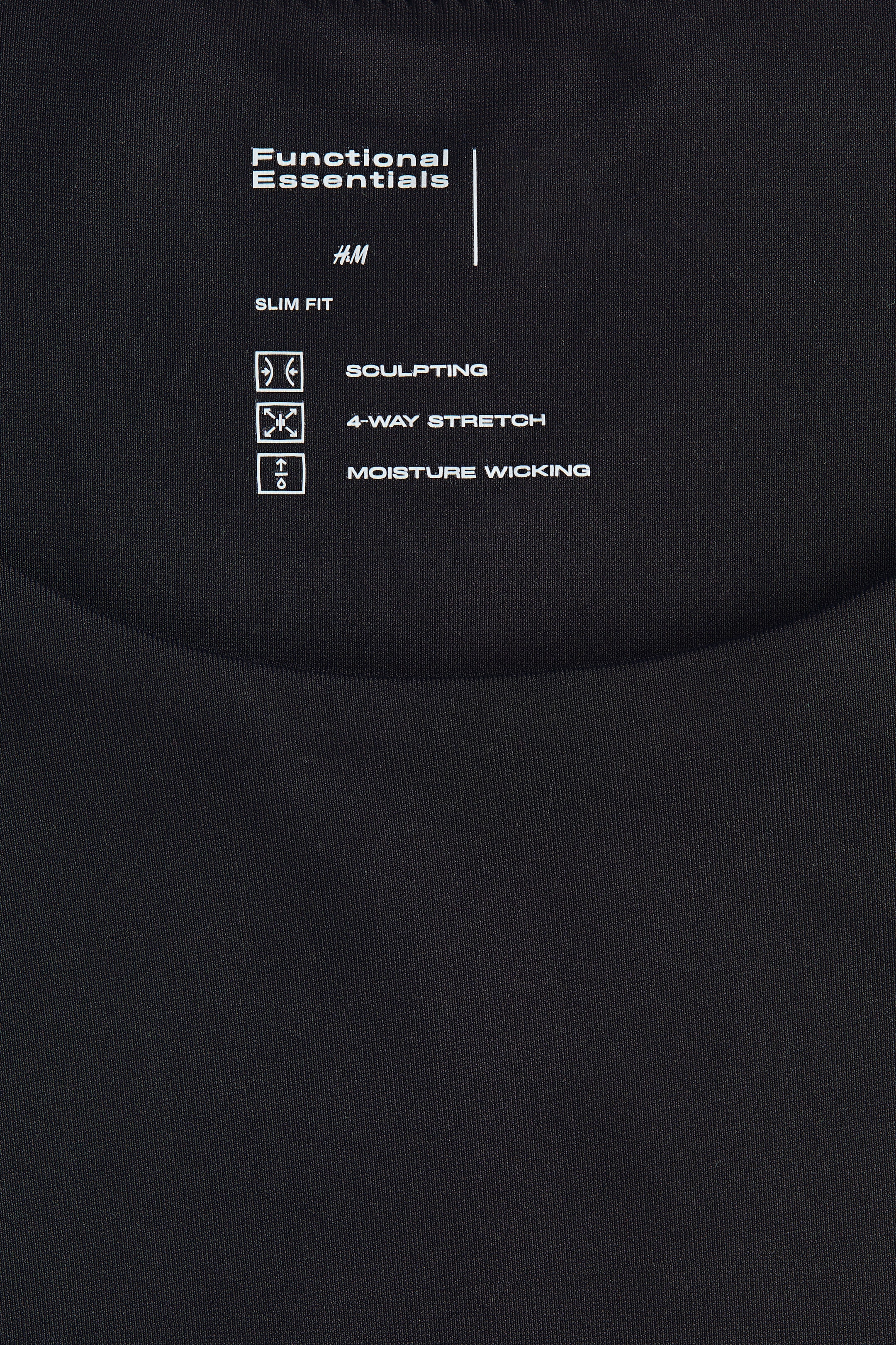 Visualizza immagine più grande: Un tessuto nero presenta un'etichetta stampata bianca sul davanti, con i dettagli "Functional Essentials", "H&M" e "Slim Fit". L'etichetta elenca anche caratteristiche come "Scolpente", "4-Way Stretch" e "Assorbimento dell'umidità", ciascuna accompagnata da un'icona specifica.