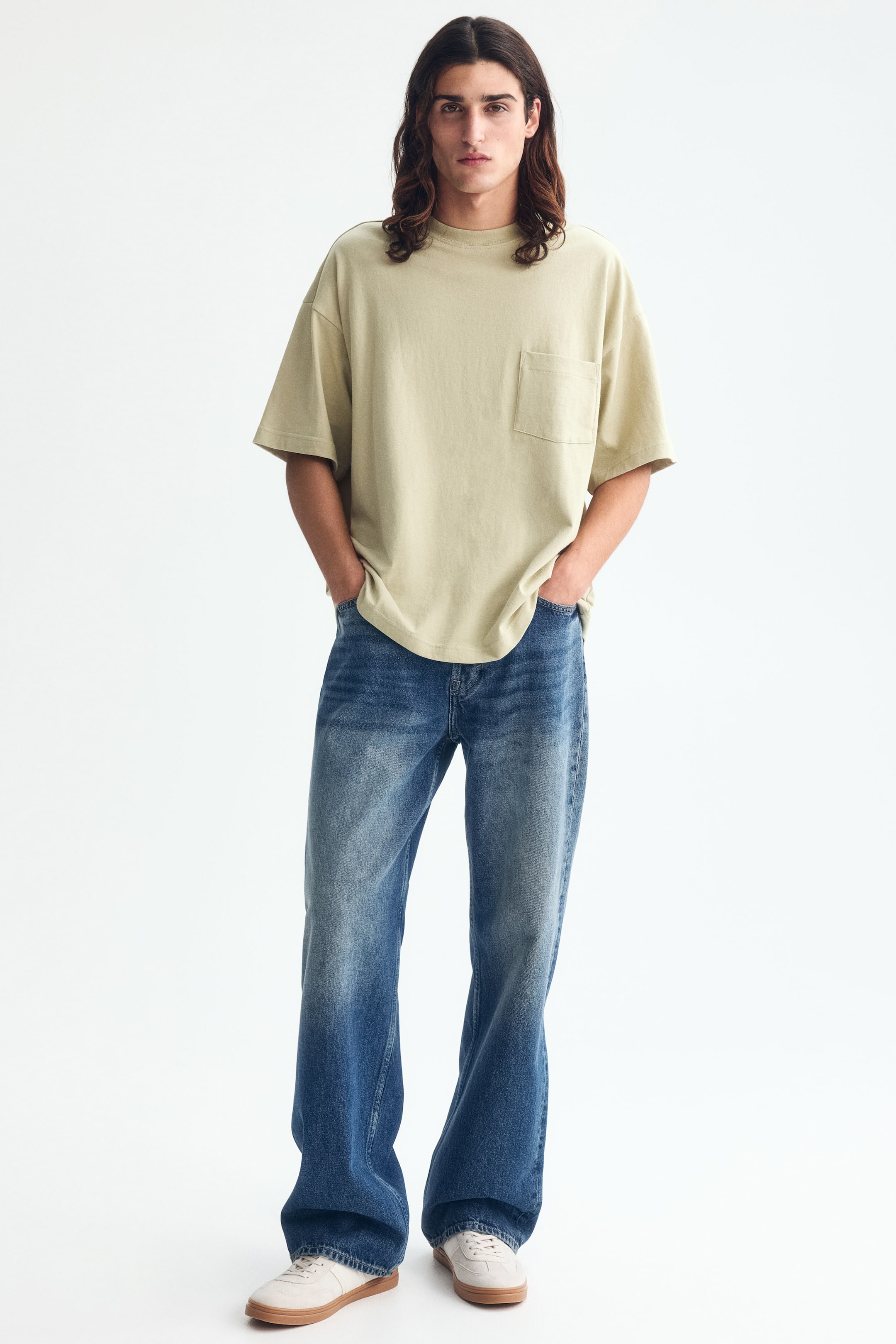 Größeres Bild ansehen: Ein blassgrünes T-Shirt wird vom Model getragen und zeigt einen runden, mit Rippbündchen versehenen Ausschnitt, überschnittene Schultern, eine Brusttasche und einen gerade geschnittenen Saum. Es präsentiert eine oversized, lockere Silhouette.