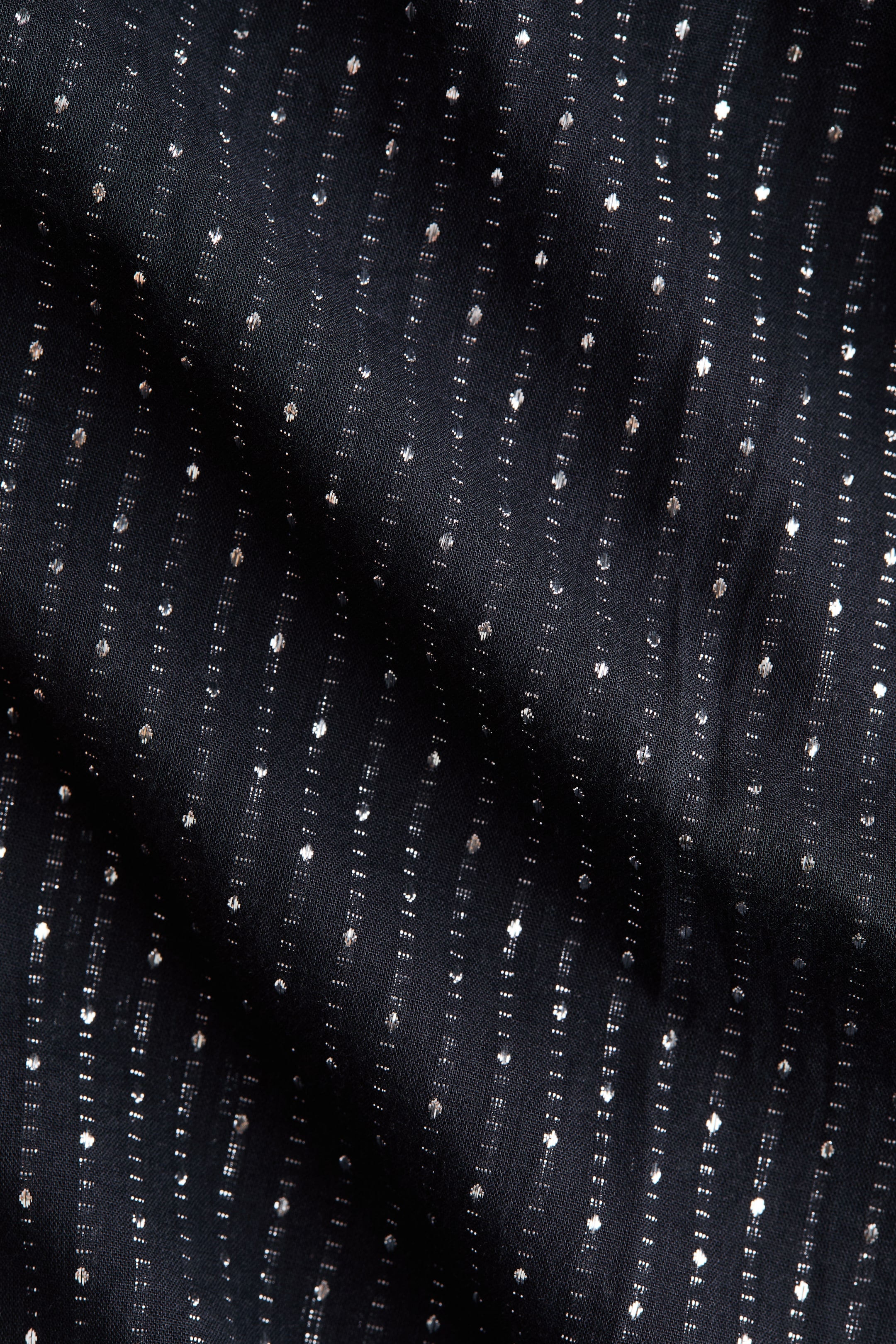 Agrandir l'image: Le tissu noir présente des rayures verticales de petits points argentés scintillants. Le matériau présente des drapés et des plis doux.