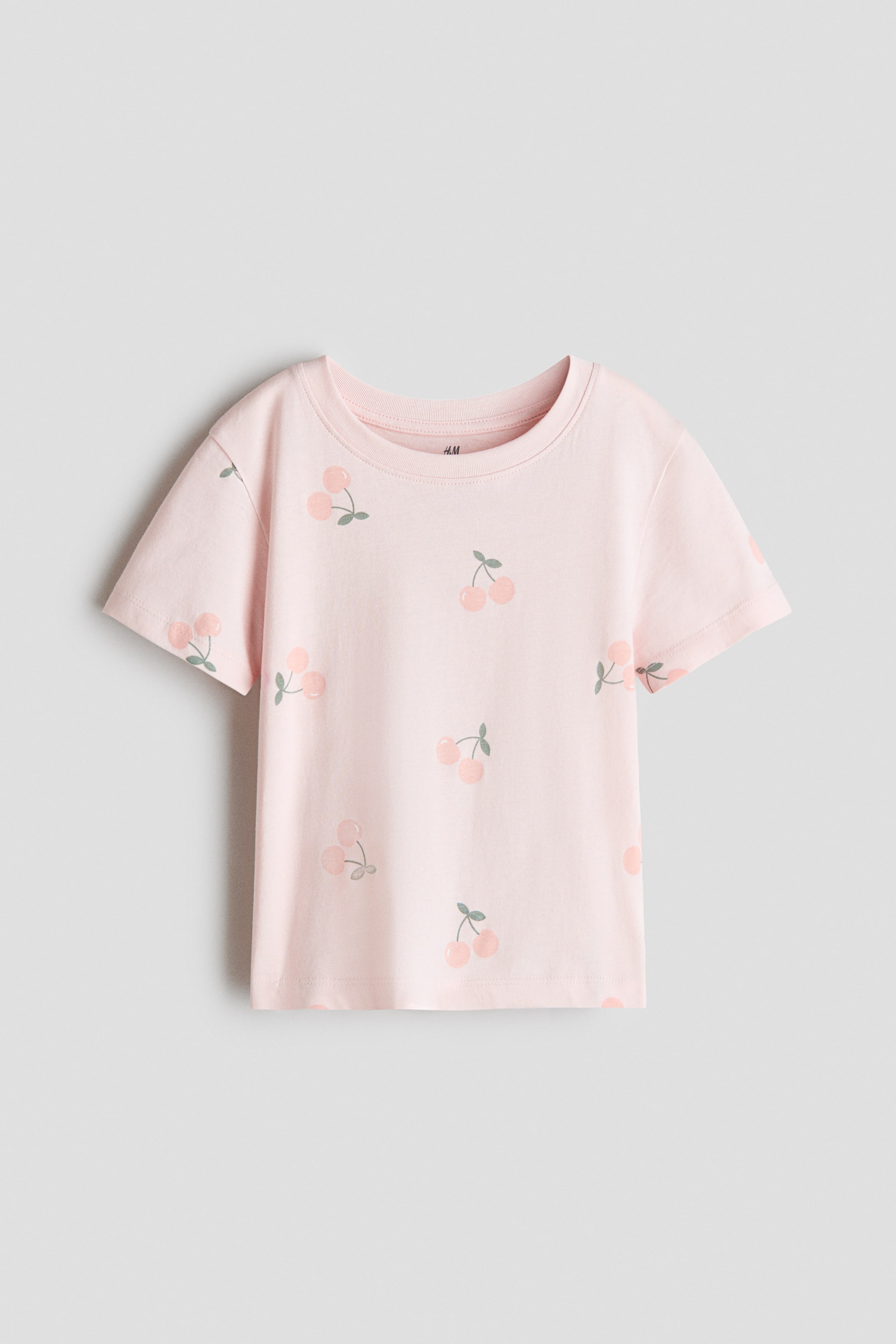 View larger image: The pink short-sleeved t-shirt showcases an all-over pattern of light pink cherries with green stems. It features a round neckline.