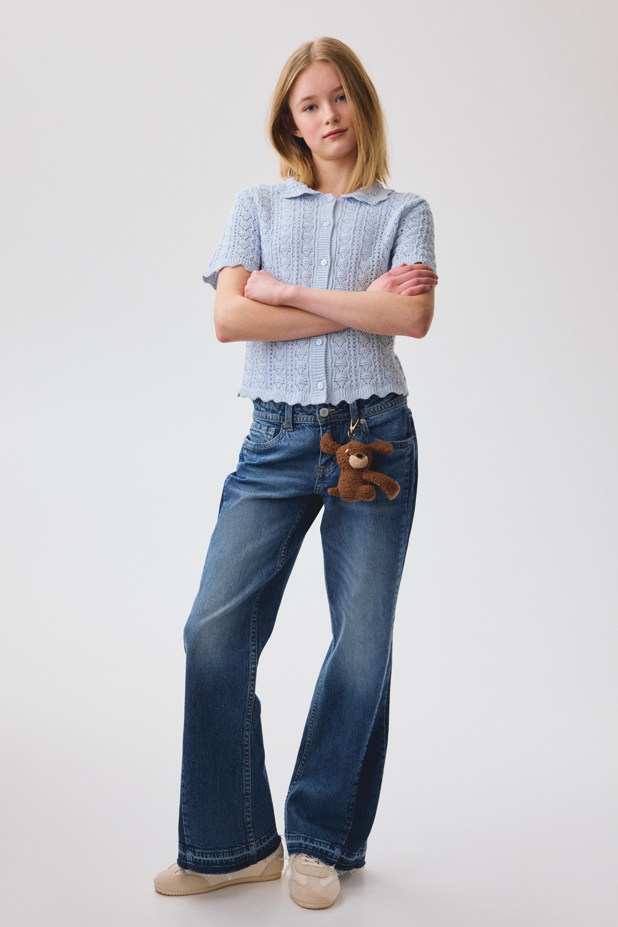 View larger image: A light blue knitted top is facing forward, featuring an openwork lace knit pattern throughout. It is designed with a scalloped collar, short sleeves, a button-front closure, and a scalloped hem.