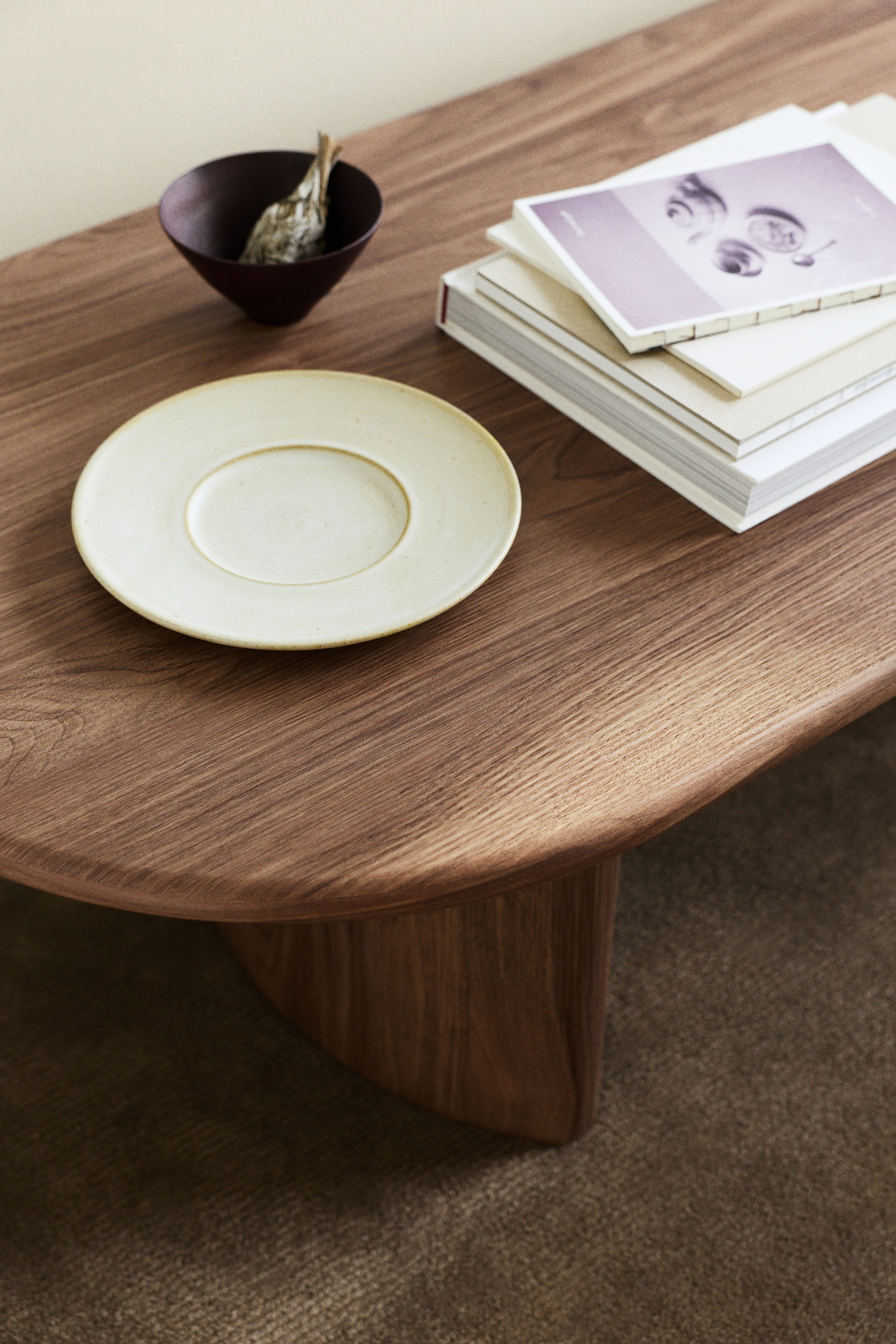 Agrandir l'image: Une grande table basse présente un plateau en bois foncé, de forme irrégulière, avec des bords doucement incurvés. Un support en bois épais et courbé soutient le plateau par en dessous.