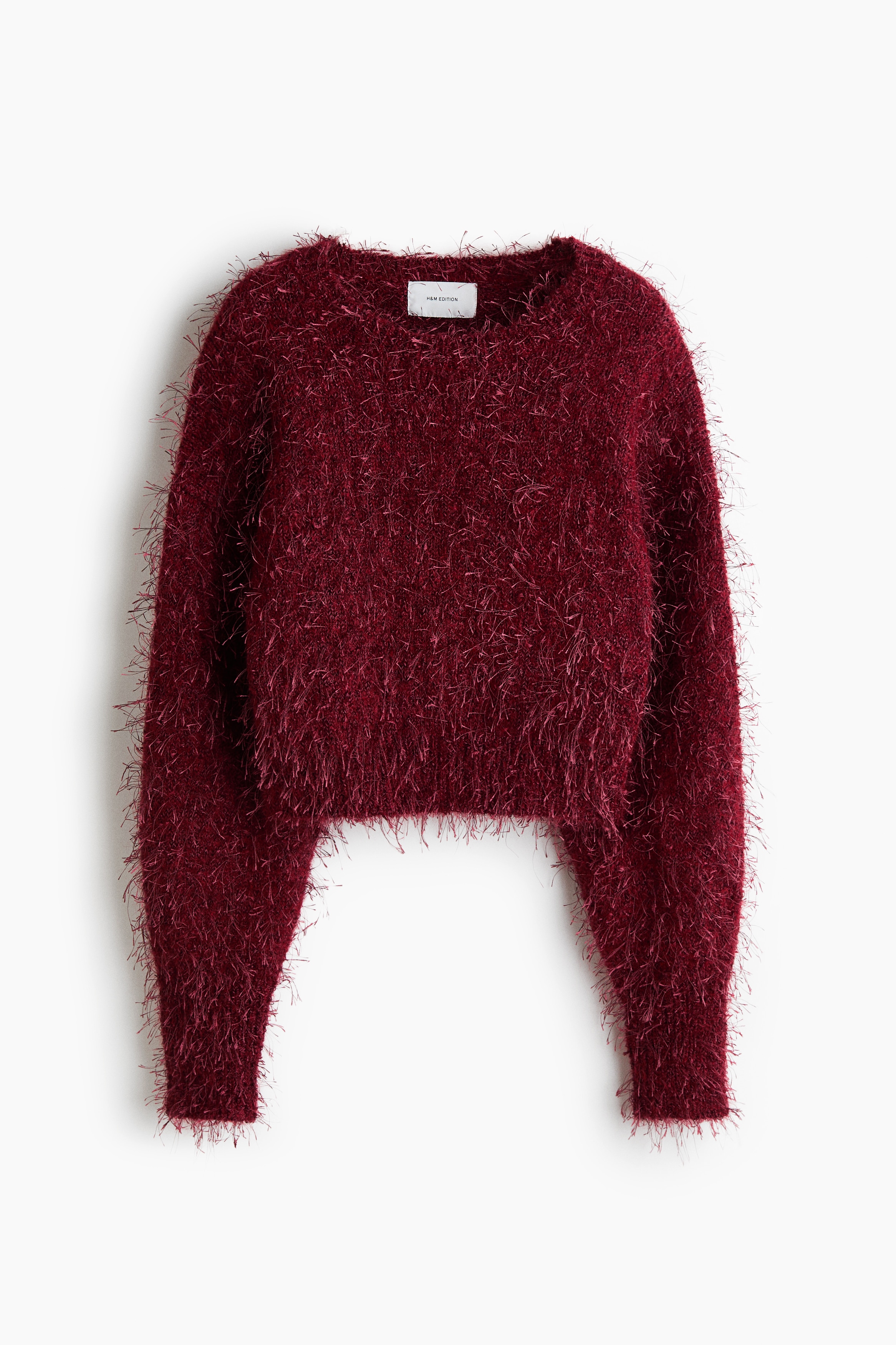 A fluffy, dark red knit jumper featuring a round neckline and long sleeves is being worn by the model. The cropped, loose-fit jumper is styled with light-blue wide-leg jeans.