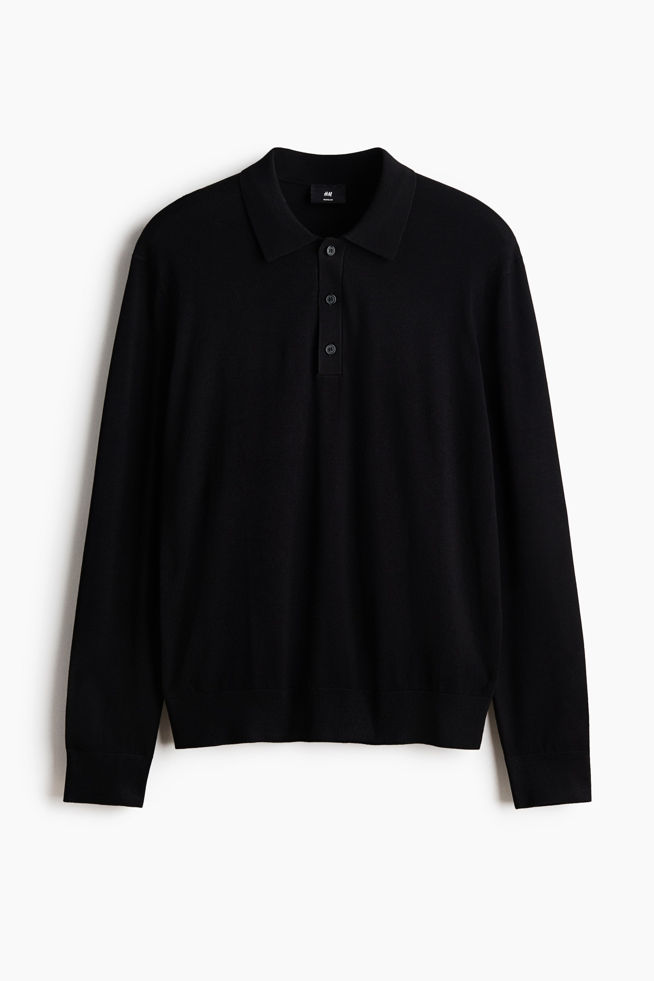 Ver imagem maior: Uma camisa polo preta de manga comprida em malha fina, com gola polo, carcela com três botões a condizer, punhos canelados e bainha canelada.