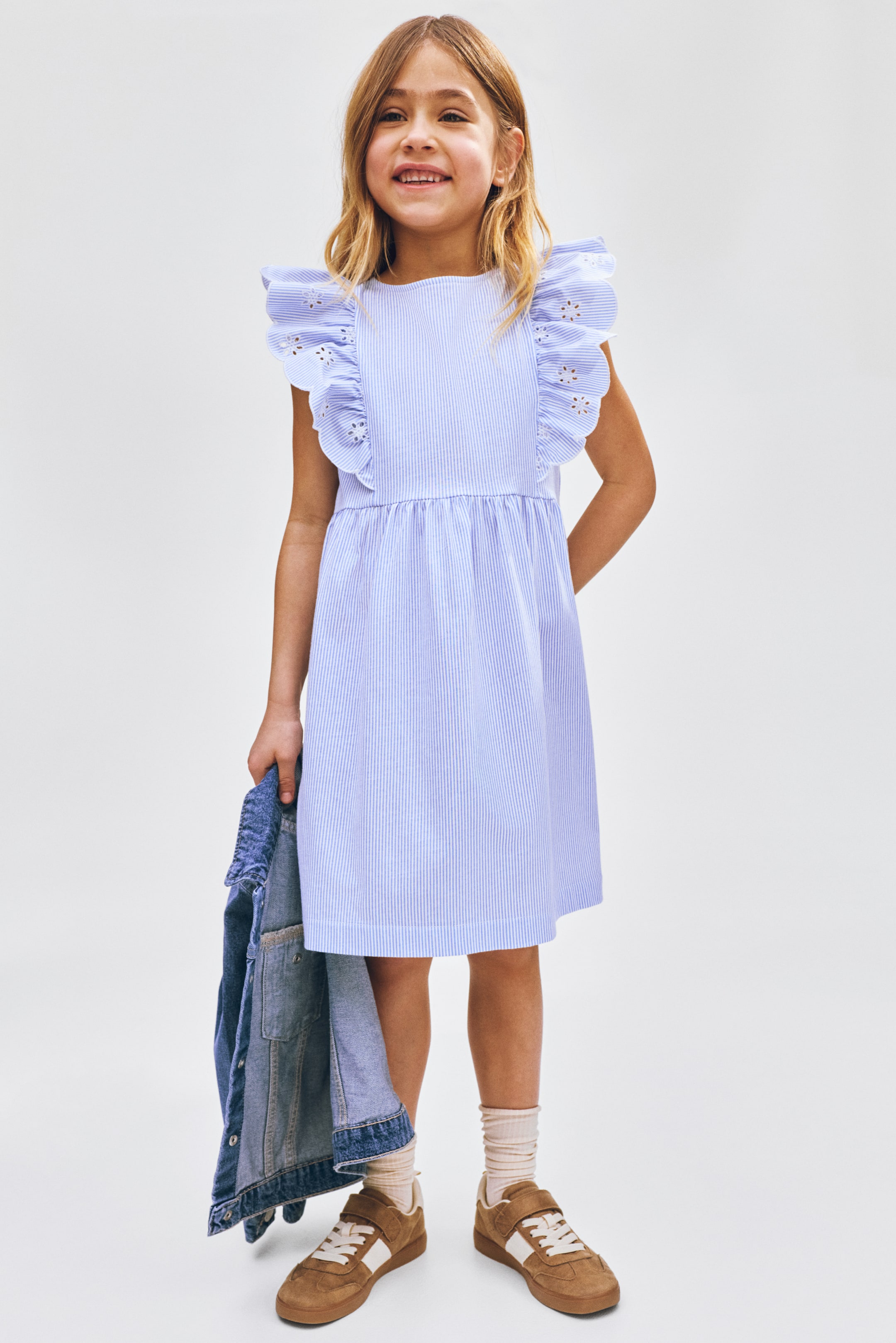 View larger image: A light blue and white vertically striped dress featuring a round neckline, ruffled cap sleeves with eyelet embroidery, a gathered waistline, and a flared skirt extending above the knee.