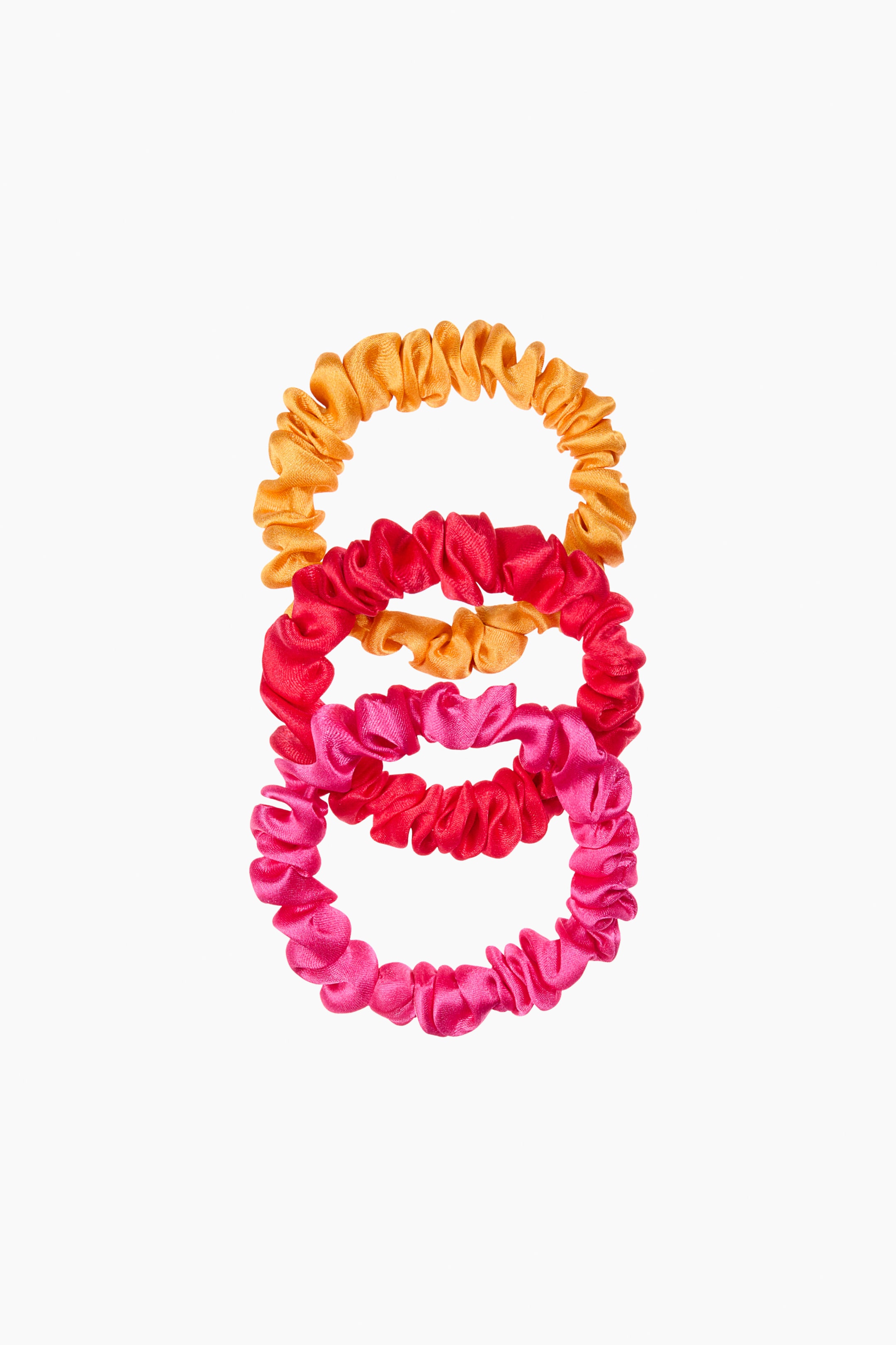Ampliar la imagen: Tres scrunchies de seda de morera elástica muestran su textura fruncida, mirando al frente. Aparecen en colores naranja brillante, fucsia y magenta, dispuestos verticalmente y ligeramente superpuestos.