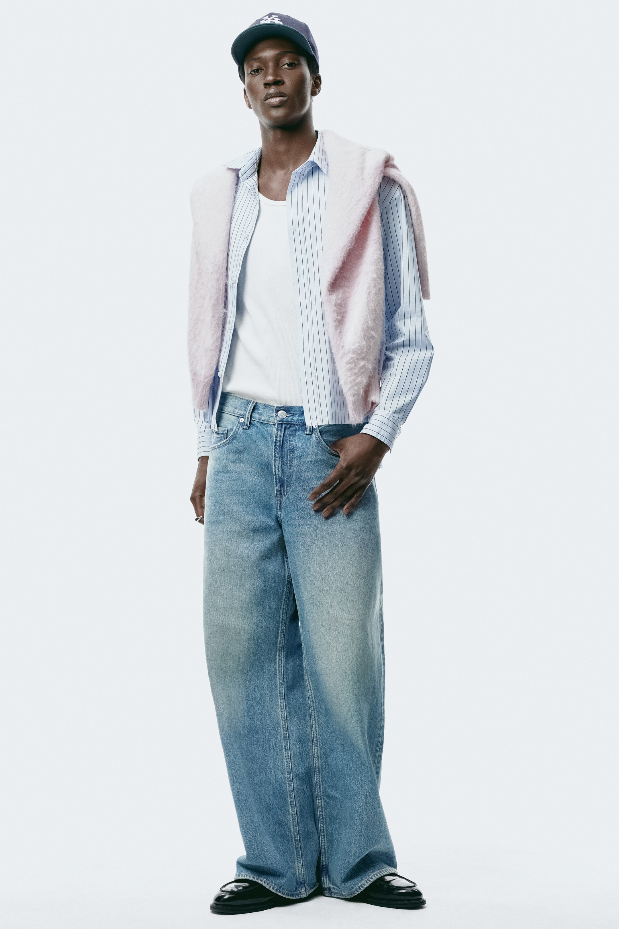 View larger image: The model is wearing 5-pocket jeans in light-wash rigid denim, featuring a regular waist, a zipper fly, a dropped crotch, and a loose, wide fit from the seat to the hem. One of the model's hands rests in a front pocket, and the jeans are styled with a tucked-in shirt and black loafers.