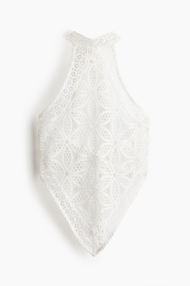 A white lace halter top is displaying an intricate floral and geometric pattern across its front, featuring a pointed hem that forms a diamond shape. - 1