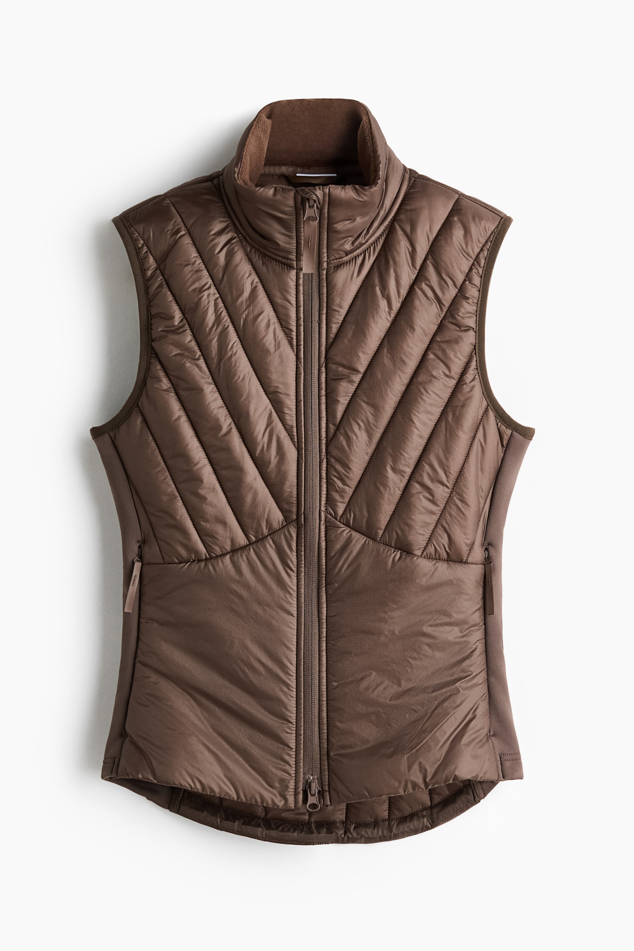 Grotere afbeelding bekijken: Sportgilet met ThermoMove heeft een bruine, gewatteerde uitvoering, gepresenteerd vanuit een vooraanzicht. Het beschikt over een ritssluiting over de volledige lengte aan de voorkant, een opstaande kraag met contrasterende fleecevoering, diagonale stiksels over de borst en schouders, horizontale stiksels aan de onderkant vooraan en gladde, ongewatteerde zijpanelen met ritszakken voor de handen.