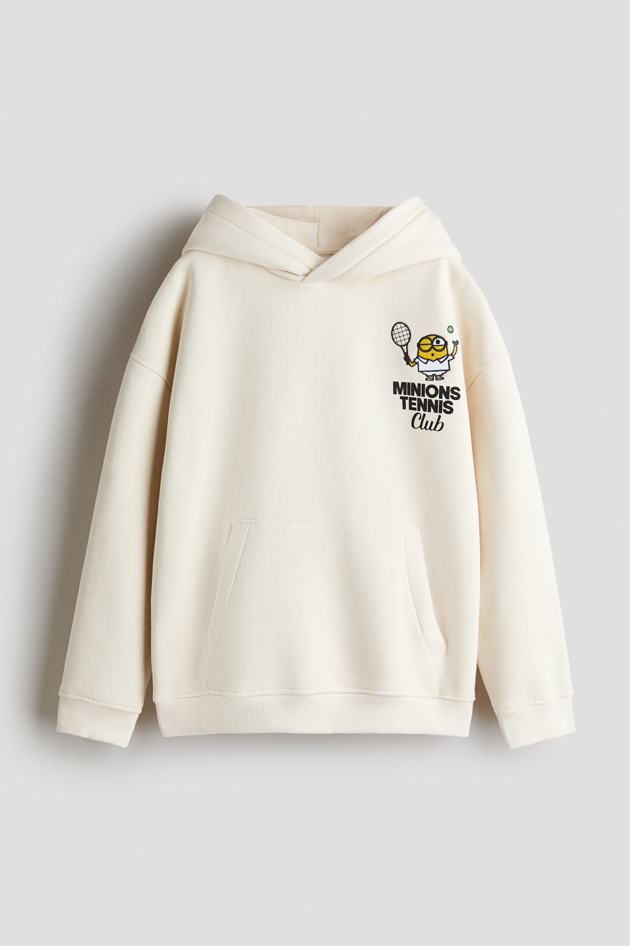 View larger image: An off-white, loose-fit hoodie is shown from the front, showcasing a wrap-front lined hood, dropped shoulders and a kangaroo pocket. The left chest features a small printed graphic of a Minion holding a tennis racket above the text "MINIONS TENNIS Club", with ribbed knit detailing finishing the cuffs and hem.