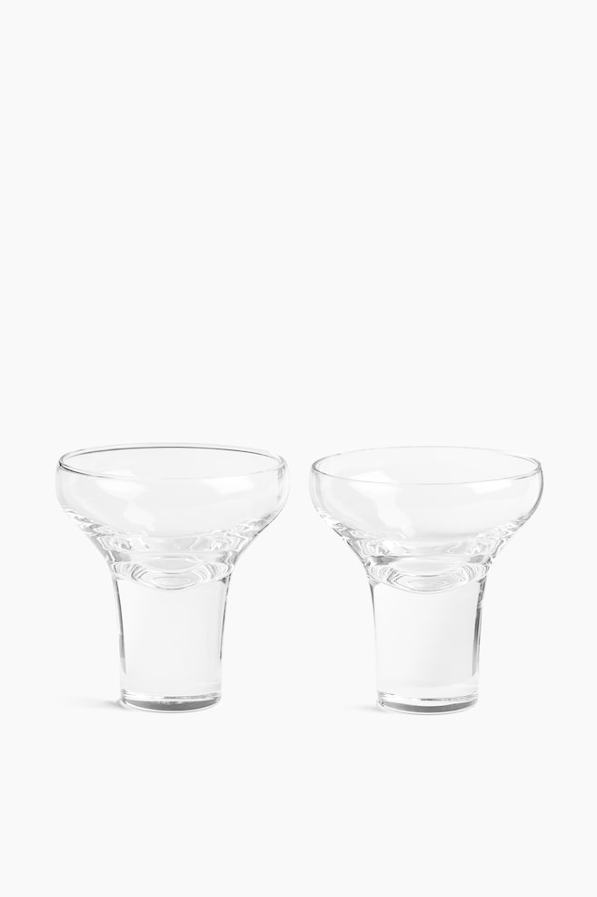 Deux coupes en verre soufflé bouche transparentes sont disposées côte à côte, mettant en valeur leurs larges coupes peu profondes et leurs bases cylindriques épaisses et pleines. Les verres sont orientés de face, soulignant leur structure transparente sans pied. - 1