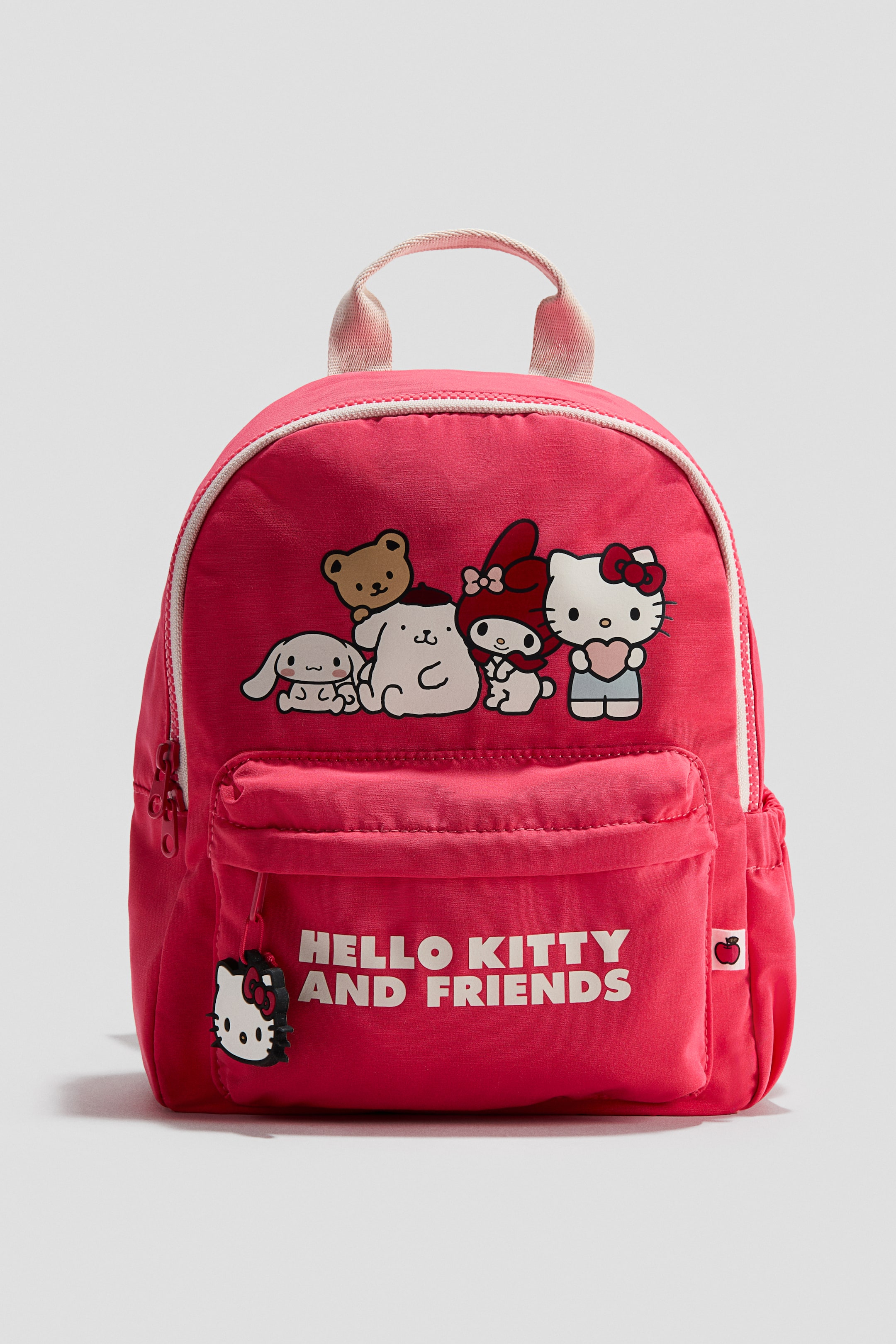 Agrandir l'image: Un mini-sac à dos rose, positionné de face, présente un imprimé graphique de Hello Kitty et de ses amis sur son compartiment principal. Une poche avant zippée affiche le texte "HELLO KITTY AND FRIENDS" et une breloque de fermeture éclair en forme de tête de Hello Kitty. Une poignée supérieure en tissu est également visible.