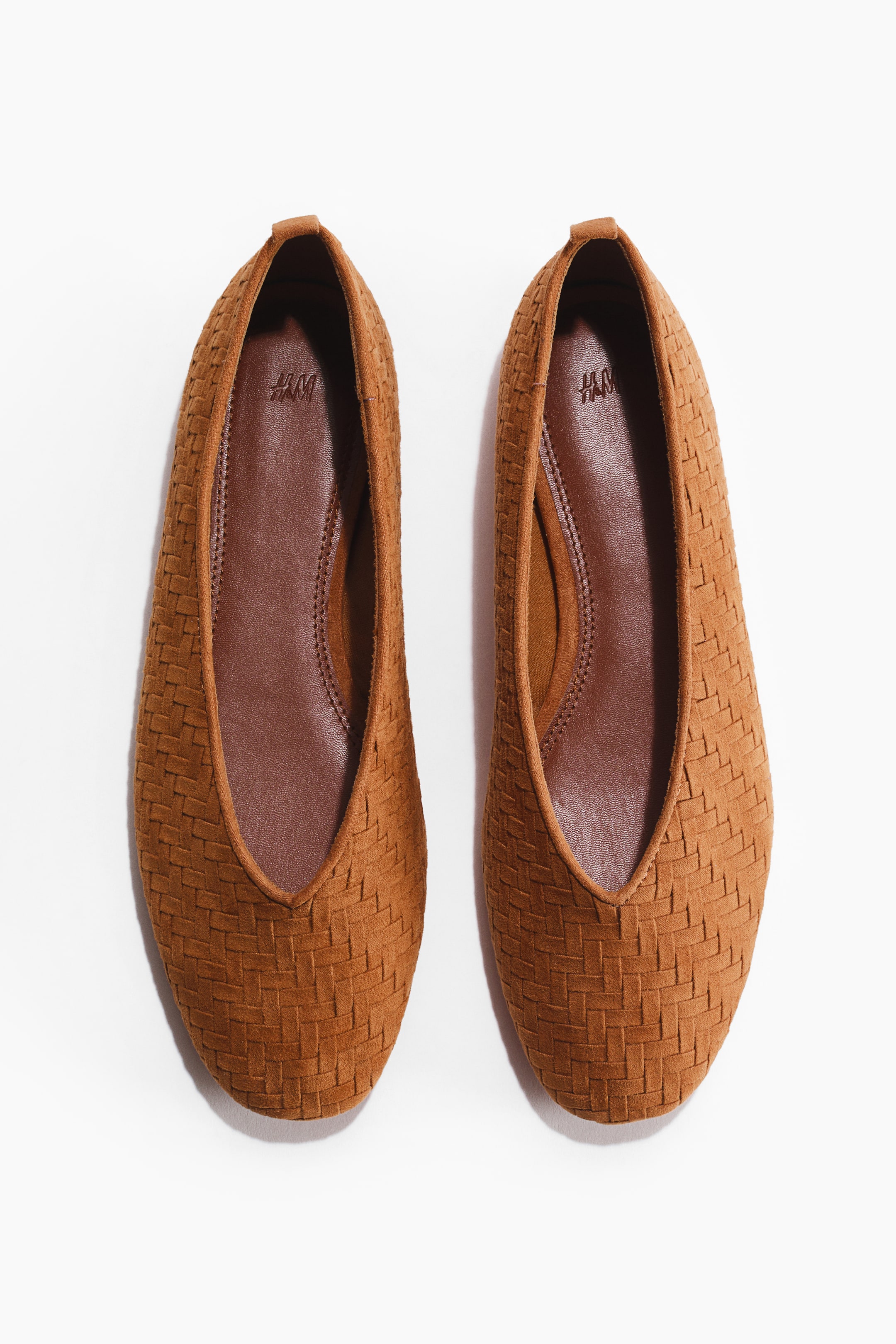 View larger image: A pair of tan-brown ballet flats featuring a braided upper, rounded toes, and a small loop at the back heel, with a dark brown lining visible inside.