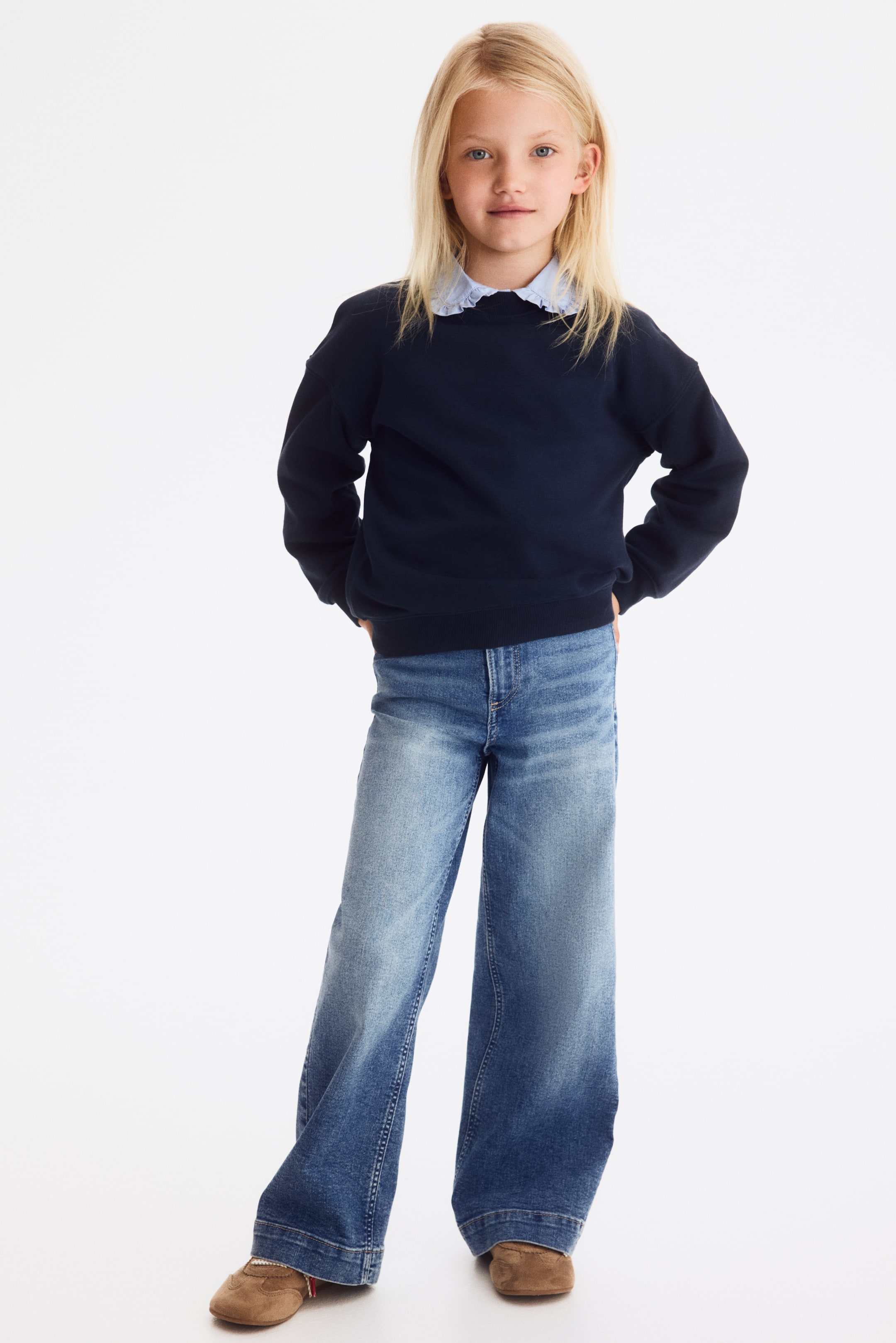 Grotere afbeelding bekijken: Jeans in stretchdenim met een slimfit door heup en dij en wijde pijpen. Vooraan is een ritssluiting zichtbaar en aan de taille een drukknoopsluiting.