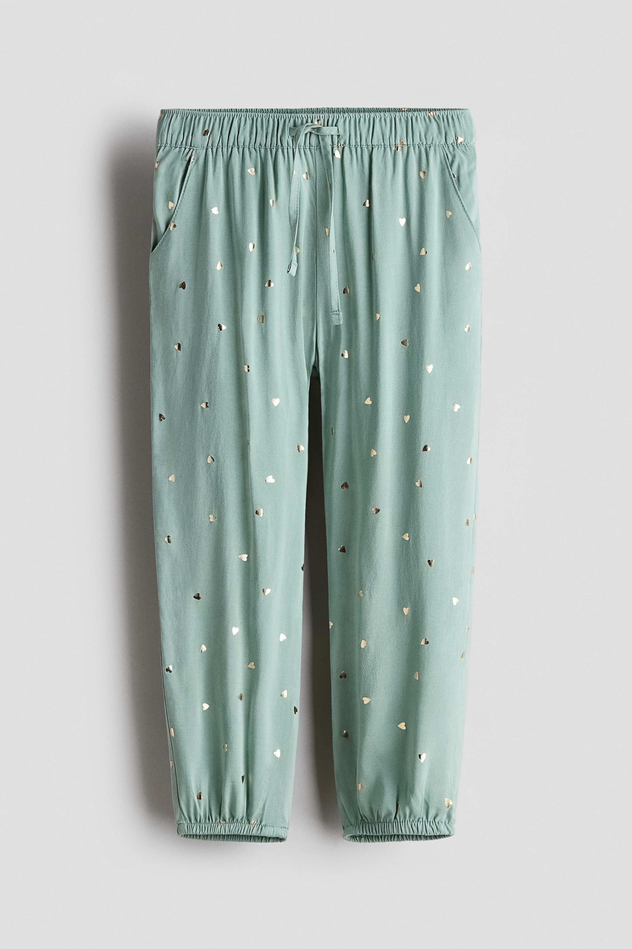 Ver imagen más grande: Los joggers muestran un tejido suave de viscosa en verde menta, estampado con pequeños corazones dorados. Se presentan en vista frontal con cintura elástica cubierta, un lazo decorativo, bolsillos laterales y bajos elásticos.