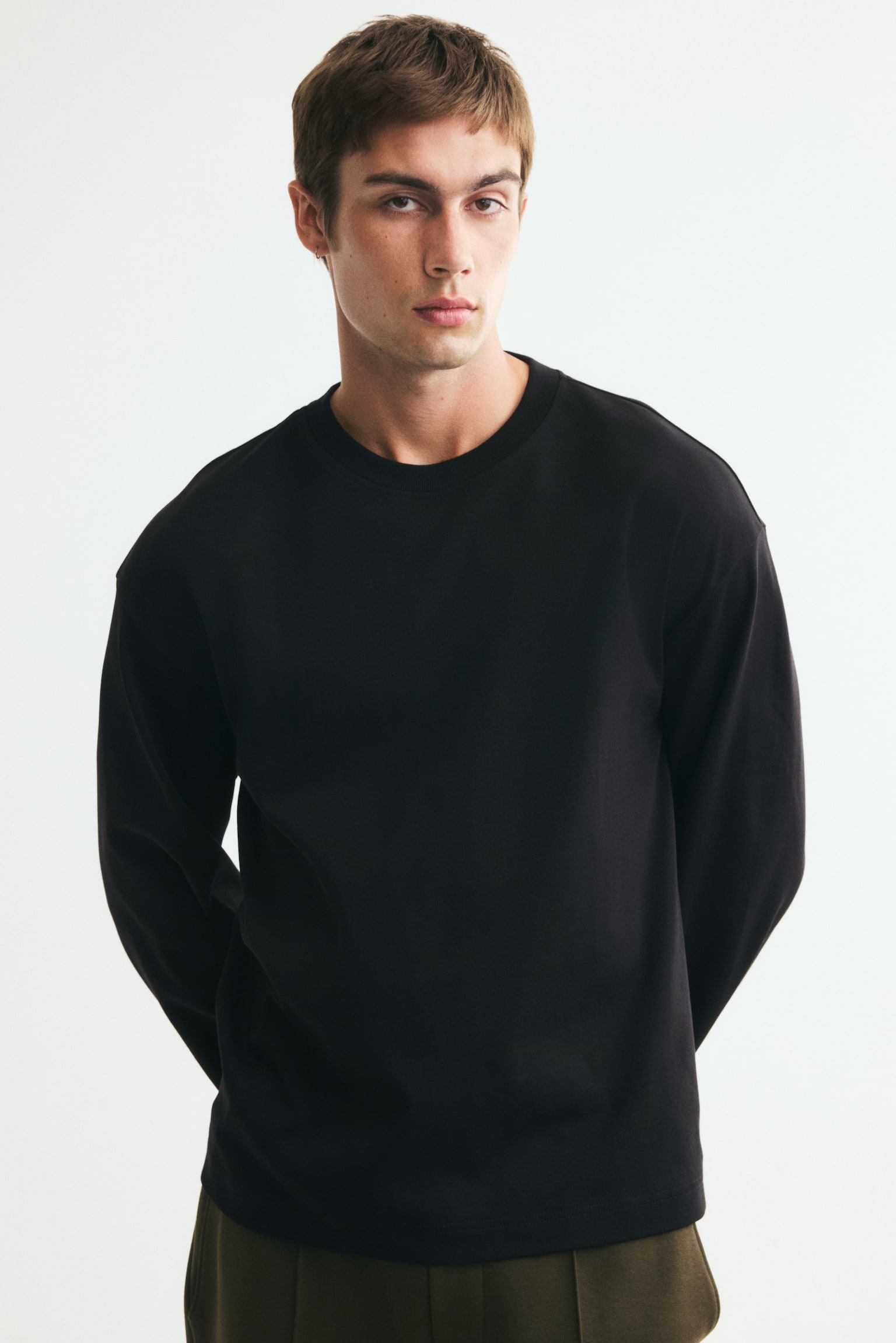 A black long-sleeved top is shown from the front, featuring a crew neck and dropped shoulders. It is designed with long sleeves and a straight, slightly cropped hem. - 1