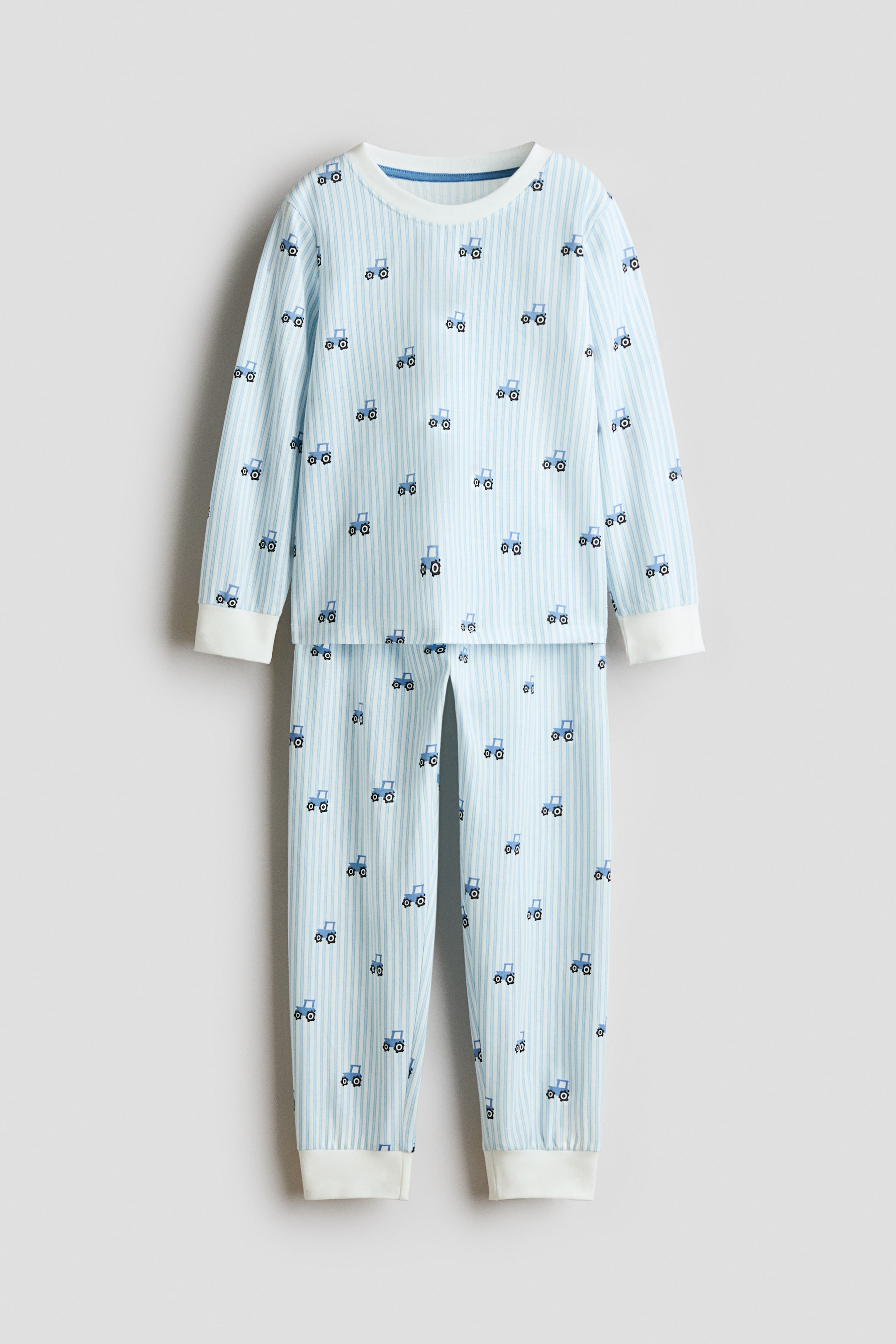 Größeres Bild ansehen: Ein Kinder-Pyjama-Set ist von vorne zu sehen und besteht aus einem langärmeligen Oberteil und einer passenden Hose in einem hellblau-weißen vertikalen Streifenmuster mit einem allover kleinen Traktor-Print. Das Oberteil ist mit einem runden Halsausschnitt mit weißer Rippblende und Rippbündchen an den Ärmeln gestaltet, während die Hose mit passenden weißen Rippbündchen an den Knöcheln versehen ist.