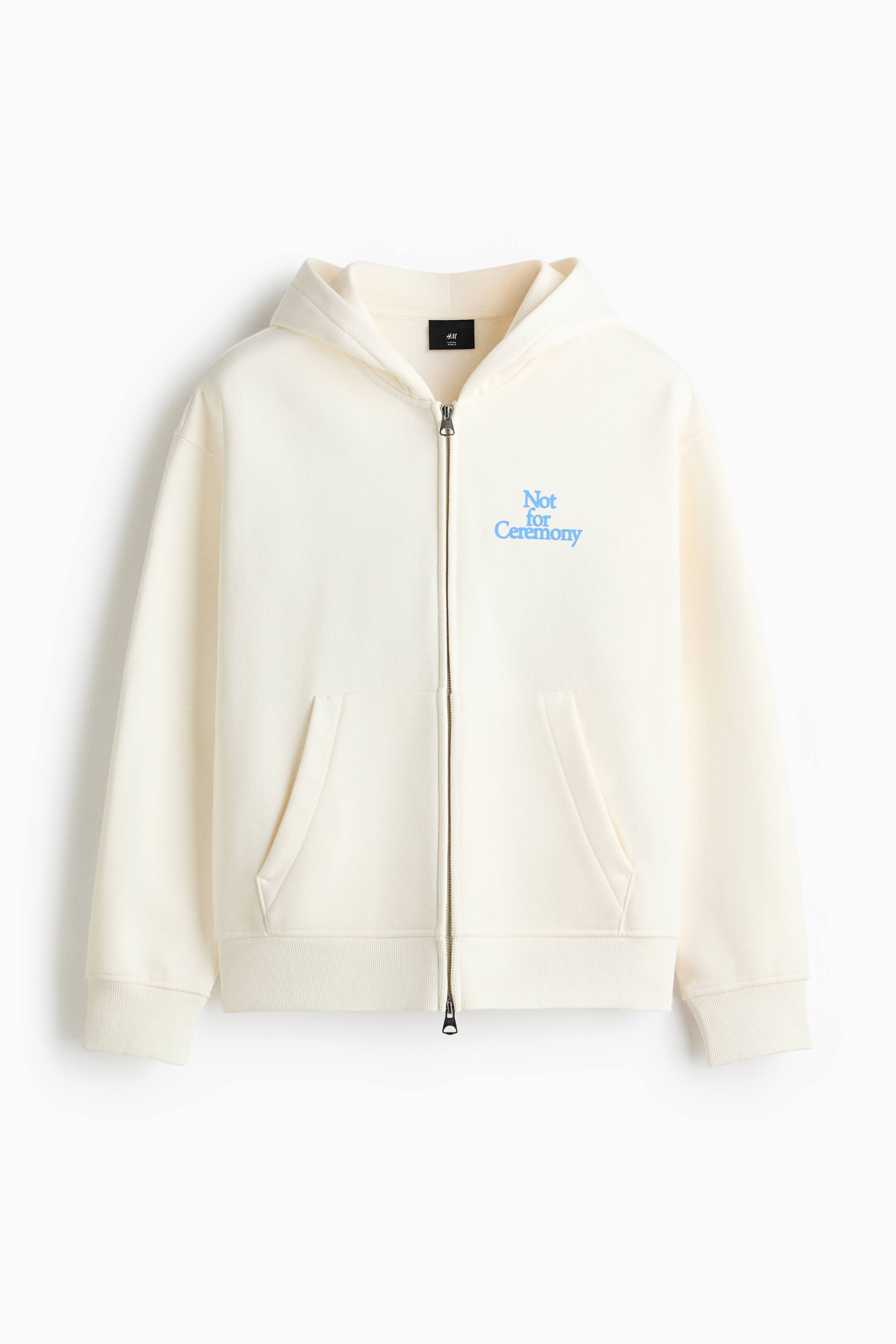 Zobacz większy obraz: Kremowa bluza z kapturem na pełny zamek jest zwrócona przodem, posiadając zapięcie na pełny zamek. Wyświetla jasnoniebieski grafik "Not for Ceremony" na lewej piersi, dwie dzielone kieszenie kangurka, prążkowane mankiety oraz prążkowany dół.