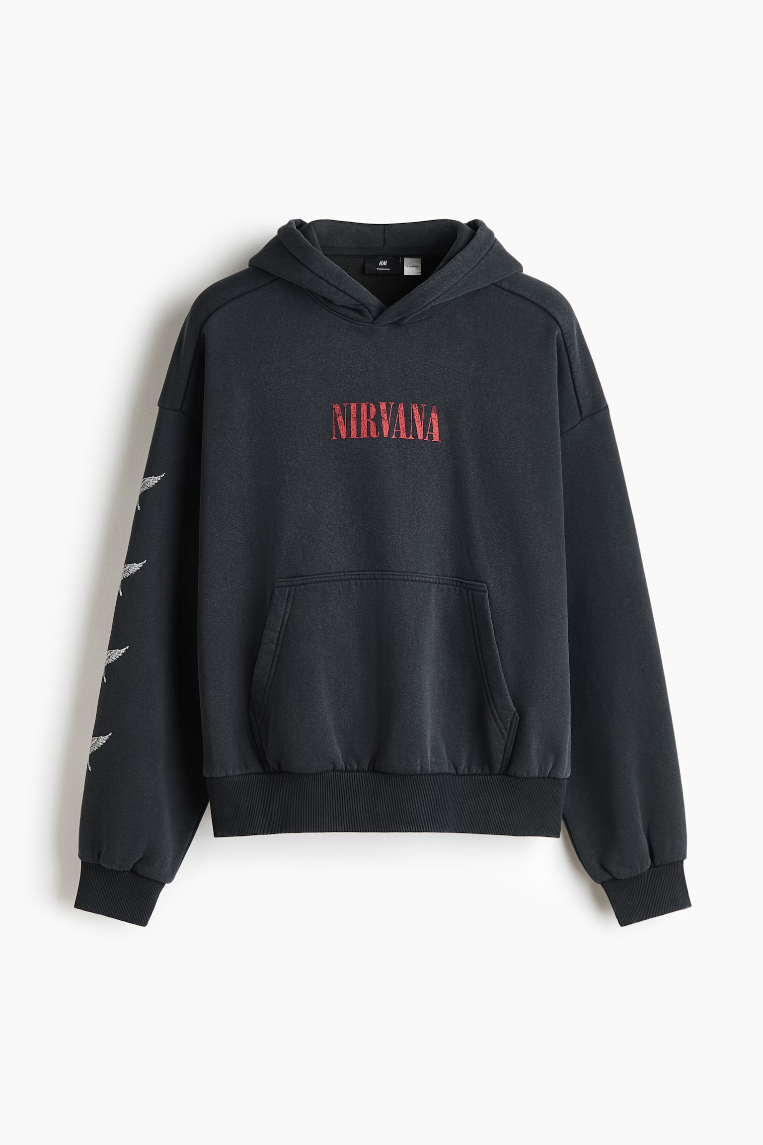 A faded black hoodie is shown from the front, featuring a distressed red "NIRVANA" graphic printed on the chest. It has dropped shoulders, a kangaroo pocket, ribbed cuffs and hem, and white wing graphics printed along the right sleeve.