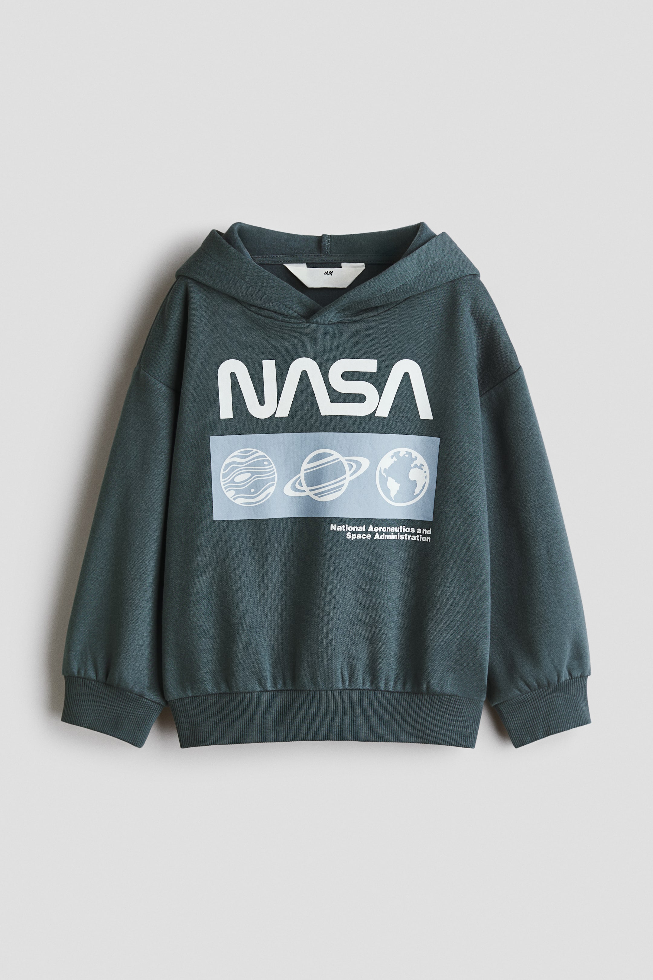 View larger image: A dark teal hoodie is laid flat, facing forward, featuring a large white "NASA" logo across the chest. Below the logo, a rectangular graphic depicts three stylized planets and the full "National Aeronautics and Space Administration" text, and the hoodie is designed with ribbed cuffs and a ribbed hem.