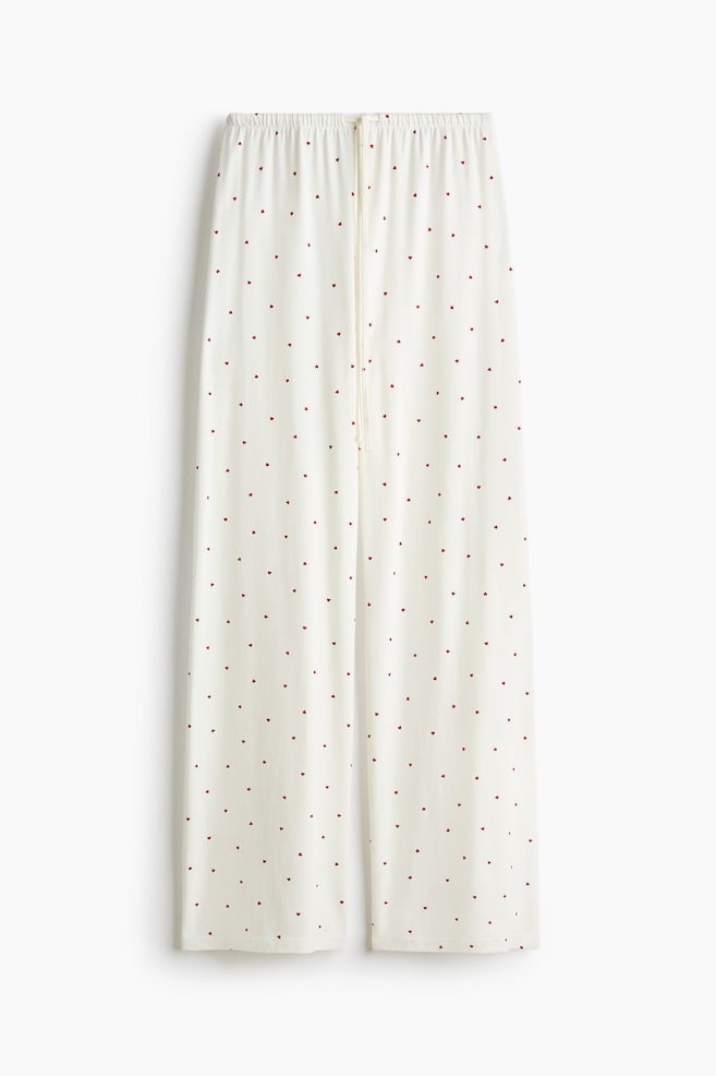 O pereche de pantaloni de pijama de culoare crem, cu croialÄ lejerÄ, este suspendatÄ cu partea din faÈÄ la vedere, evidenÈiind un imprimeu integral cu inimioare roÈii mici. Pantalonii au talie elasticÄ Ã®ncreÈitÄ, cu Ènur subÈire de reglare, Èi cracuri largi, cu croialÄ lejerÄ. - 1
