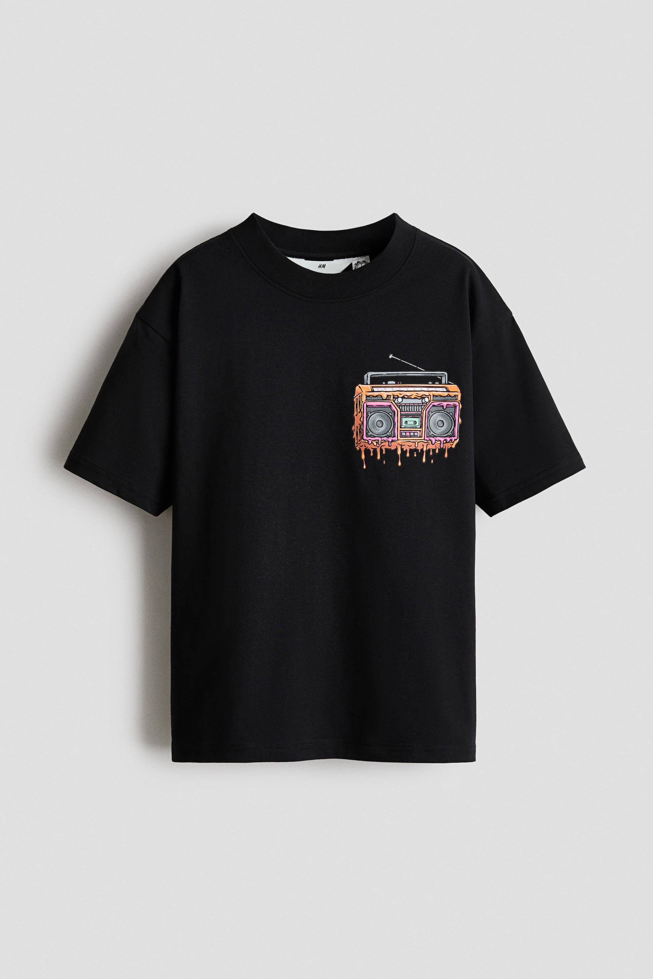 Größeres Bild anzeigen: Ein schwarzes Baumwoll-Jersey-T-Shirt ist von vorne zu sehen und zeigt einen gerippten Besatz am Halsausschnitt. Es verfügt über ein buntes Boombox-Motiv auf der Brust, das einen tropfenden Farbeffekt zeigt, und präsentiert einen lockeren Schnitt mit überschnittenen Schultern.