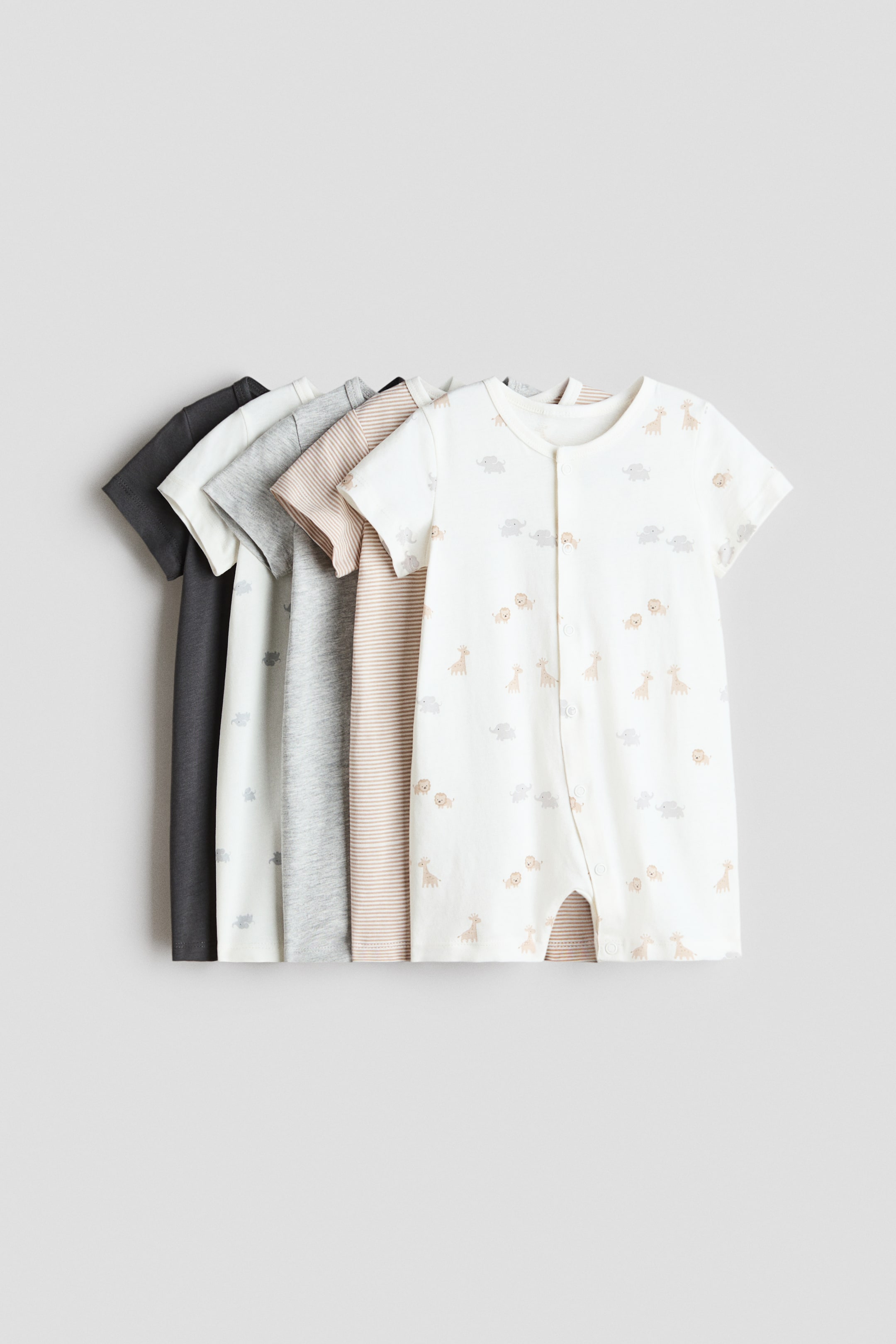View larger image: Five baby rompers are displayed, layered one behind the other. The front romper is an off-white, short-sleeved, short-legged design, featuring a rounded neckline, a full-length front snap placket, and snap closures at the leg openings. It is patterned with small cartoon elephants, giraffes, and lions. Partially visible rompers appear behind it in dark gray, light gray, a gray marl, and a beige and white stripe.