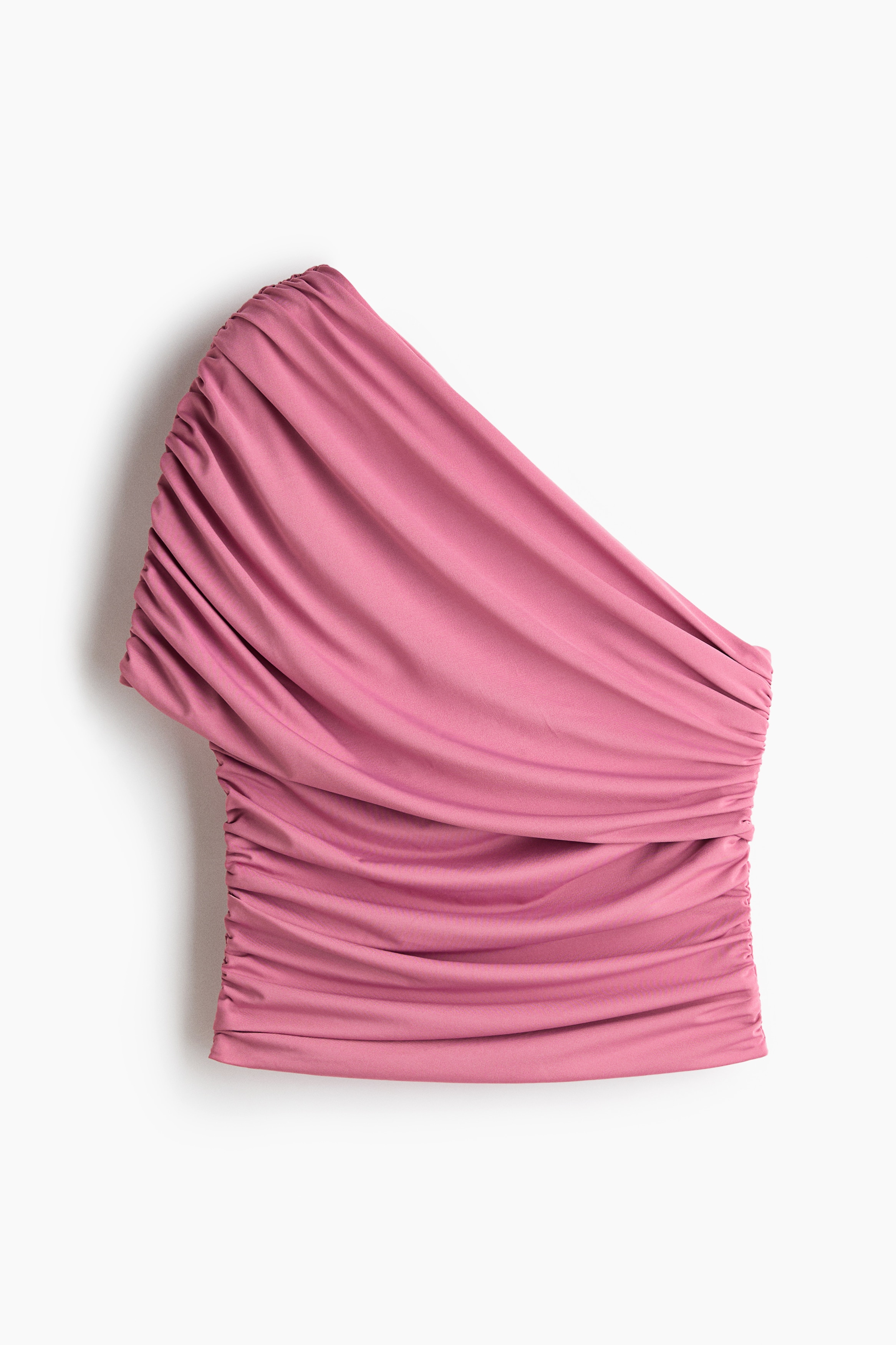 A pink, one-shoulder cropped top featuring draped and gathered detailing is being worn by the model. The top is styled with high-waisted, wide-leg black trousers, and the model is holding a black fringed clutch.