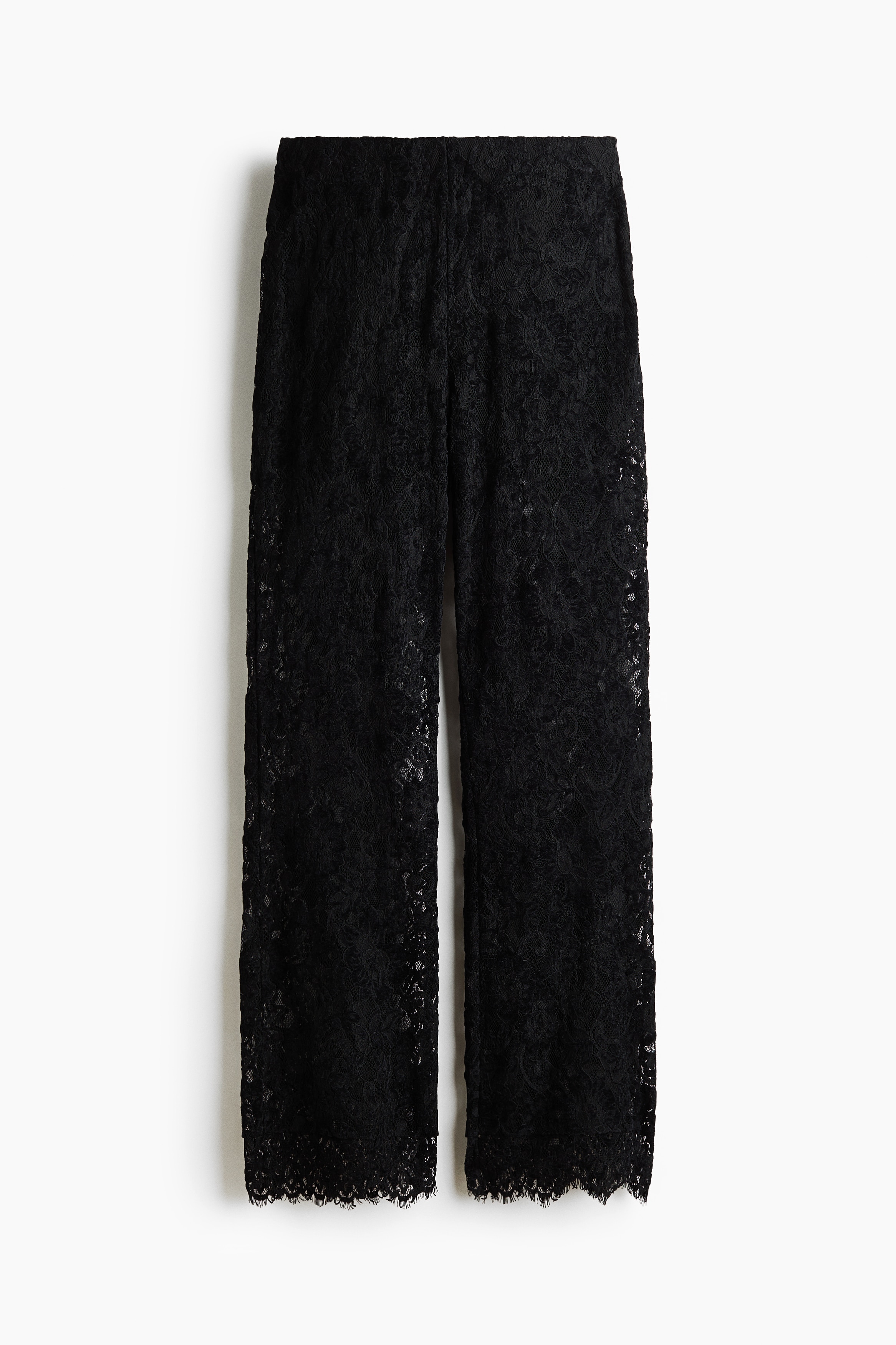 The model is wearing black lace trousers featuring a fitted silhouette and gently flared hems with scalloped, eyelash-stitch edges. The trousers are styled with a matching black lace short-sleeved top.
