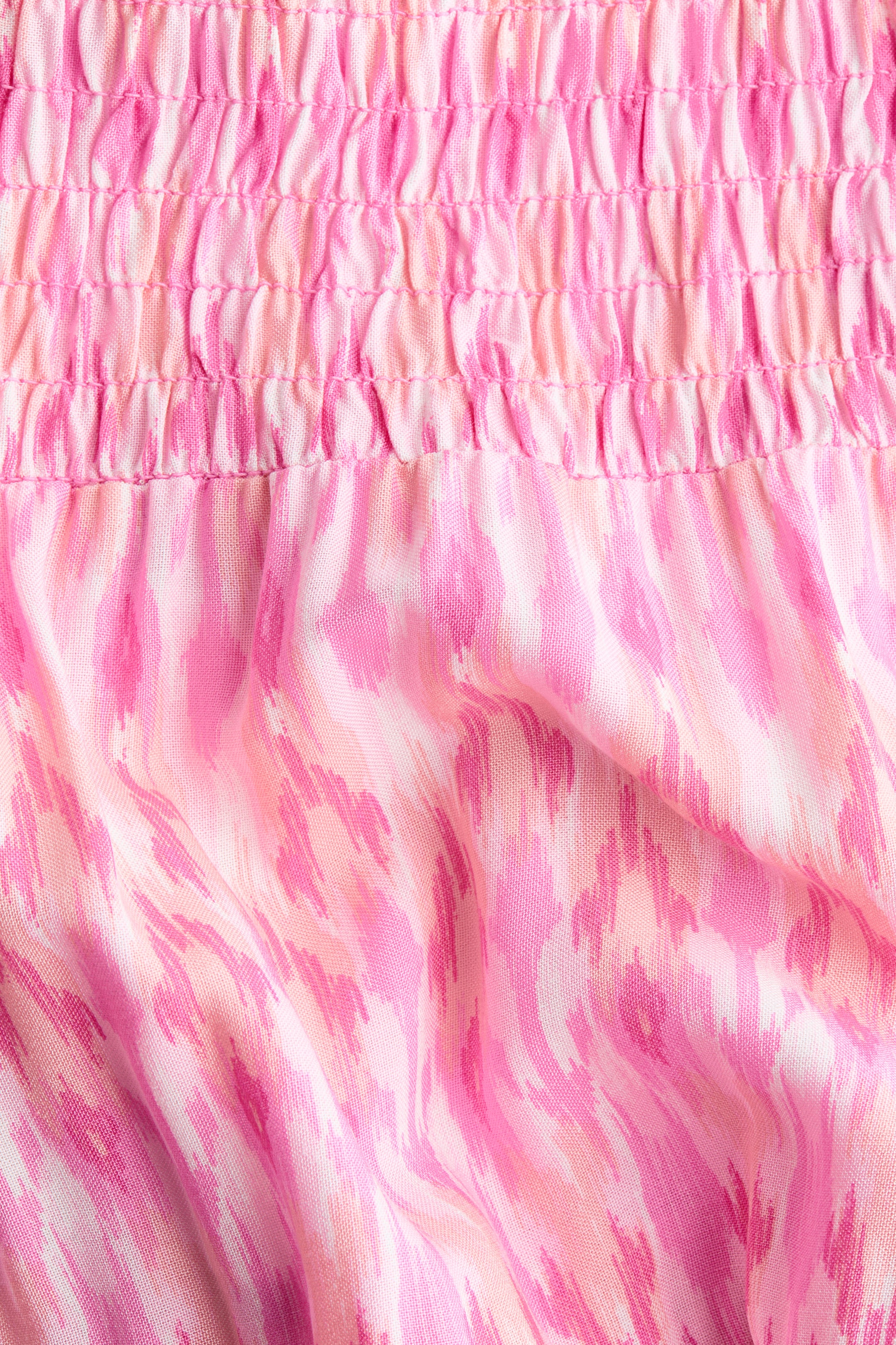 Größeres Bild ansehen: Ein Rock mit einem gesmokten Bund am oberen Ende. Der Rockkörper unterhalb des Bunds zeigt ein abstraktes Muster in verschiedenen Rosa- und Weißtönen und besteht aus einem luftigen Webstoff.
