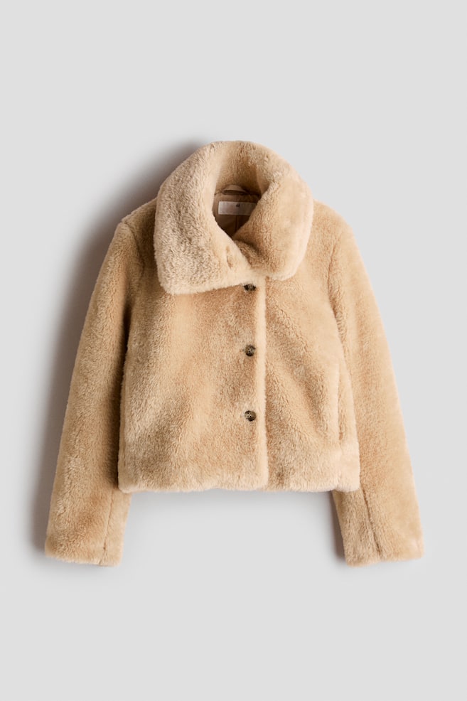 Eine beigefarbene Kunstfelljacke ist von vorne zu sehen und verfÃ¼gt Ã¼ber einen flauschigen, breiten Kragen, eine kurze Silhouette und einen dreifachen Frontverschluss mit KnÃ¶pfen. Die Jacke zeigt lange, gerade Ãrmel und eine weiche, strukturierte OberflÃ¤che rundum. - 1