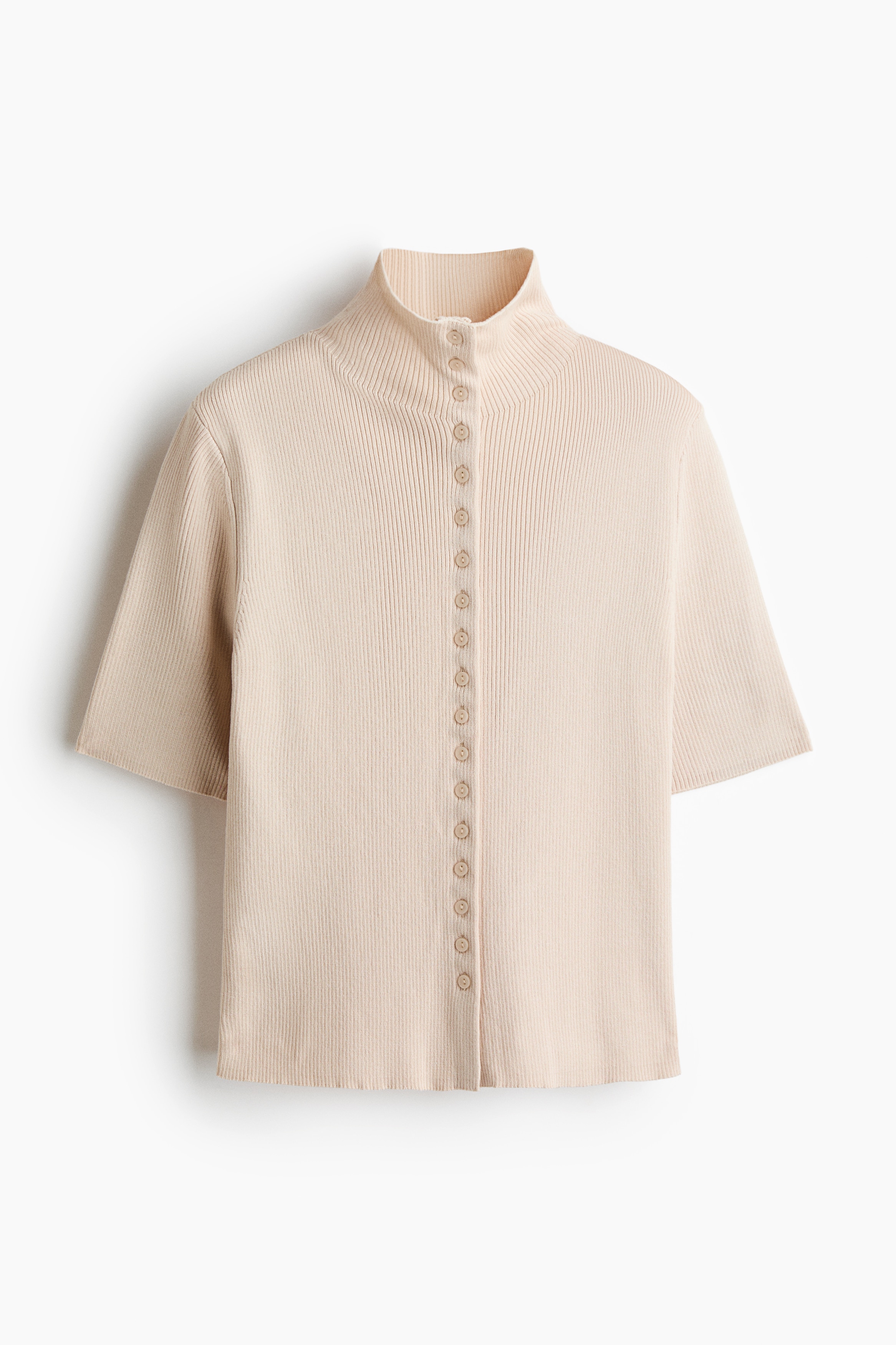 A cream-colored, rib-knit fitted cardigan featuring a high neck, short sleeves, and a button-down front is being worn by the model. The cardigan is styled with white pants, with the bottom few buttons left unfastened.