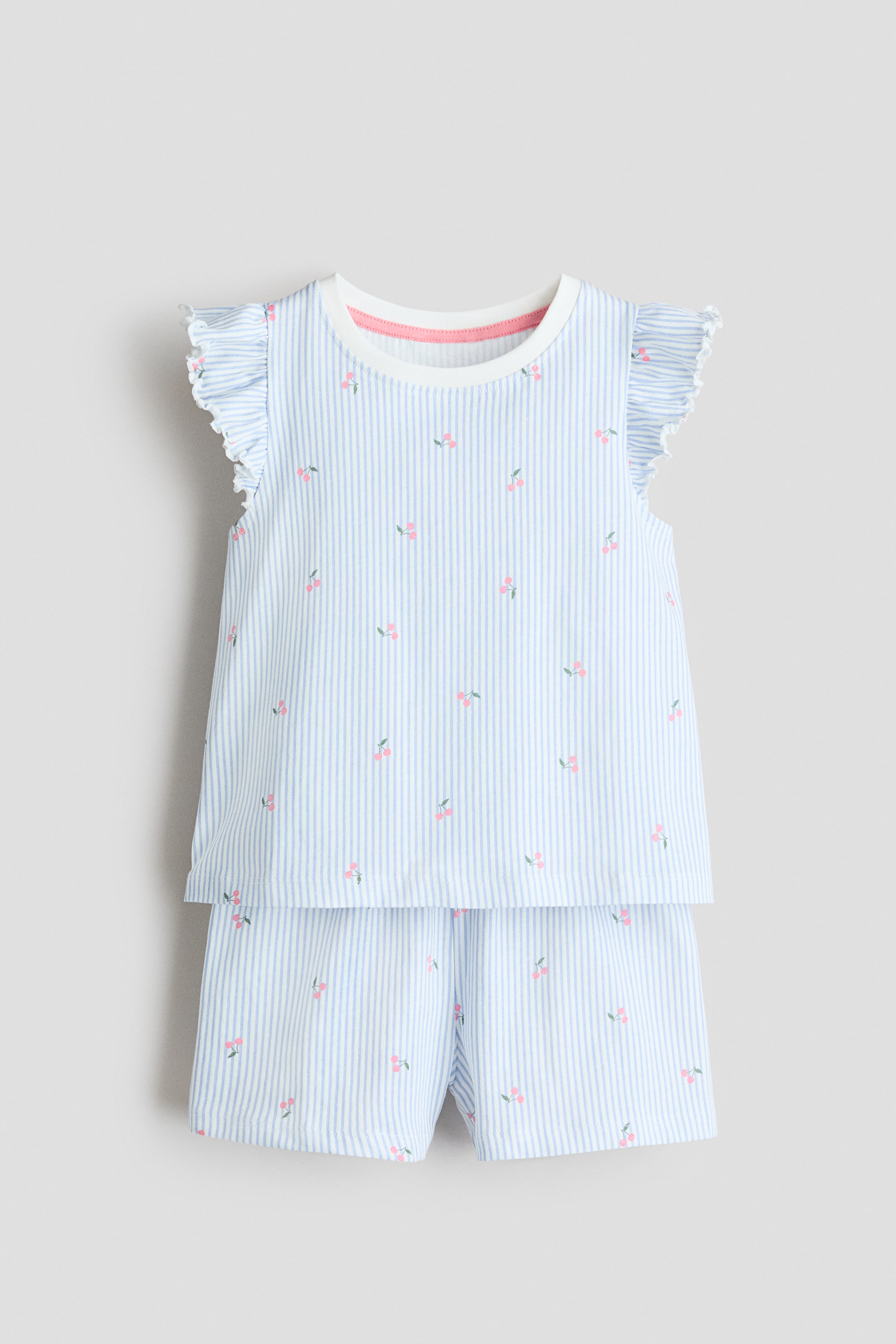 View larger image: A two-piece pyjama set is shown from the front, featuring light blue and white vertical stripes with small pink cherry motifs. The top has a white ribbed round neck, a pink inner neckline trim and ruffled cap sleeves, paired with matching shorts to complete the set.