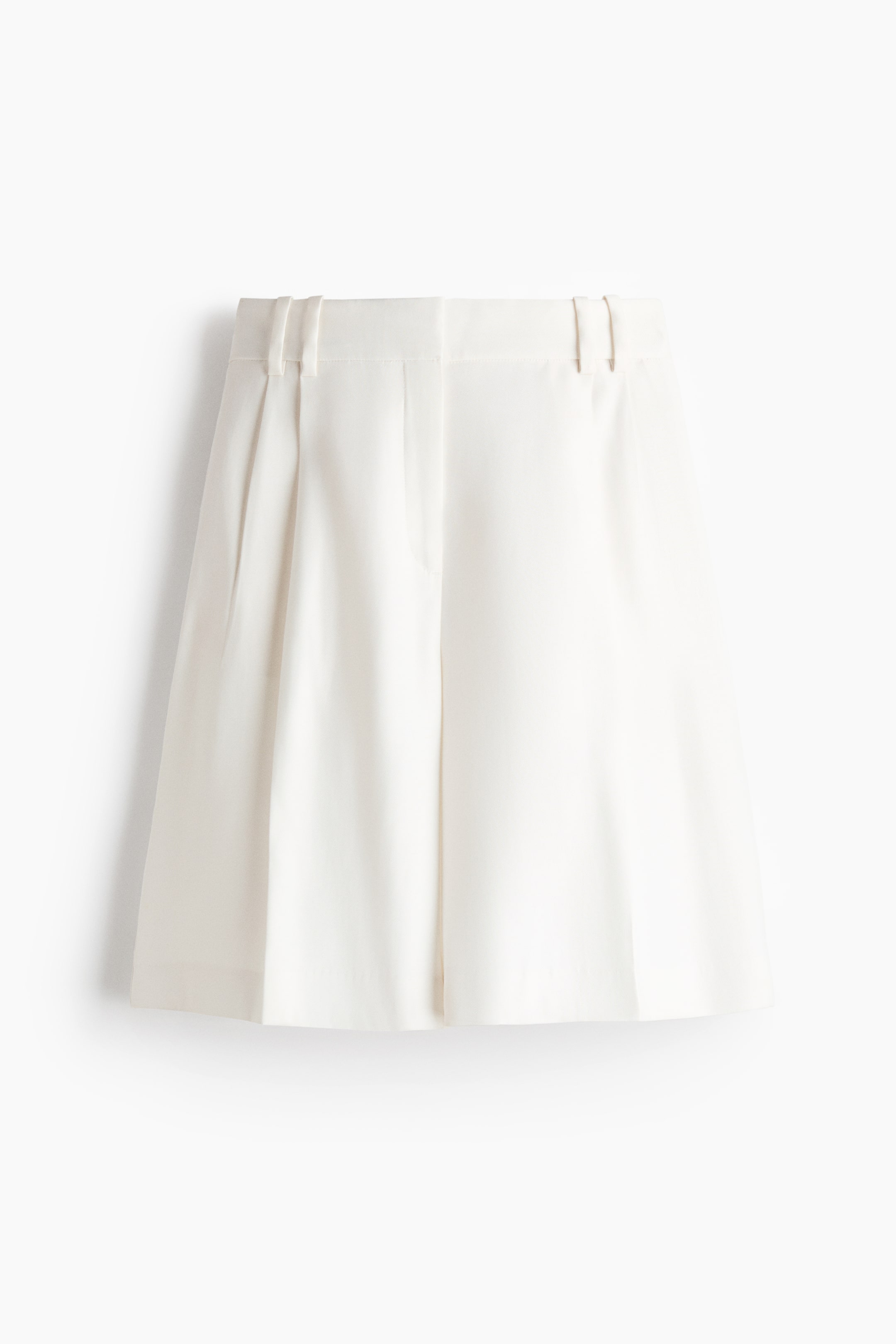 Ver imagen más grande: Los pantalones cortos blancos están mostrando su vista frontal, con una cinturilla plana con trabillas y dos pliegues frontales visibles en el lado izquierdo. También se muestra un cierre de cremallera, y los pantalones cortos presentan un corte de pierna ancha con un dobladillo recto.
