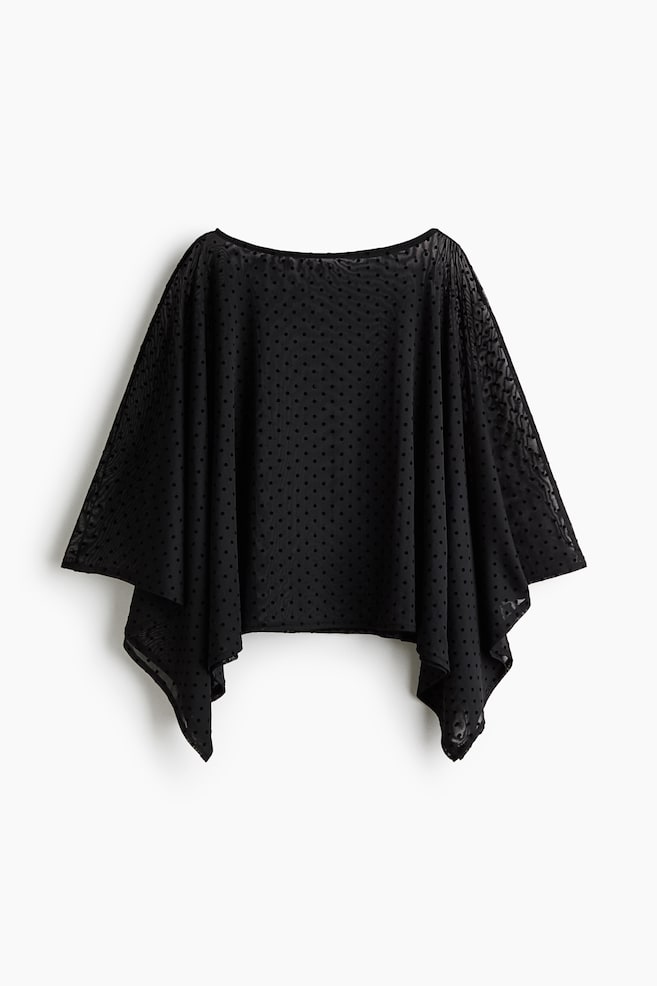 A black sheer poncho-style top is shown from the front, featuring an all-over small polka-dot pattern and a wide boat neck. The fabric is draping loosely at the sides to form a flowing, handkerchief hem with pointed corners. - 1